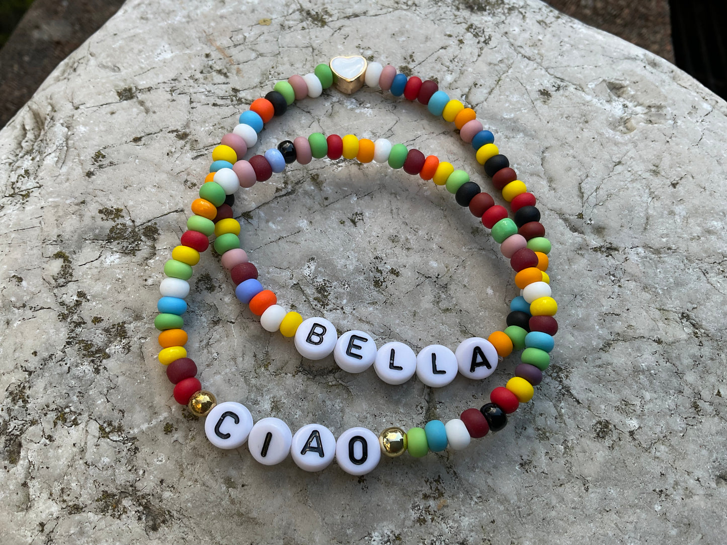 Zwei bunte Armbänder mit den Worten Ciao und Bella mit einer Herzperle