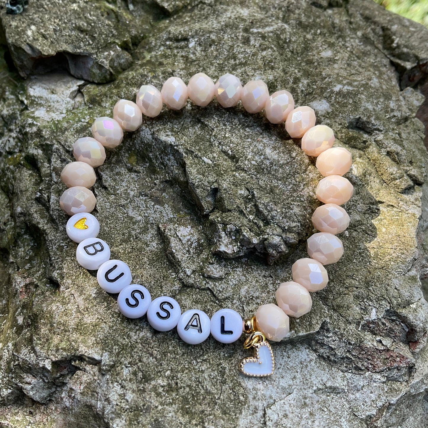 Ein cremefarbenes Perlenarmband mit Bussal und Herzanhänger