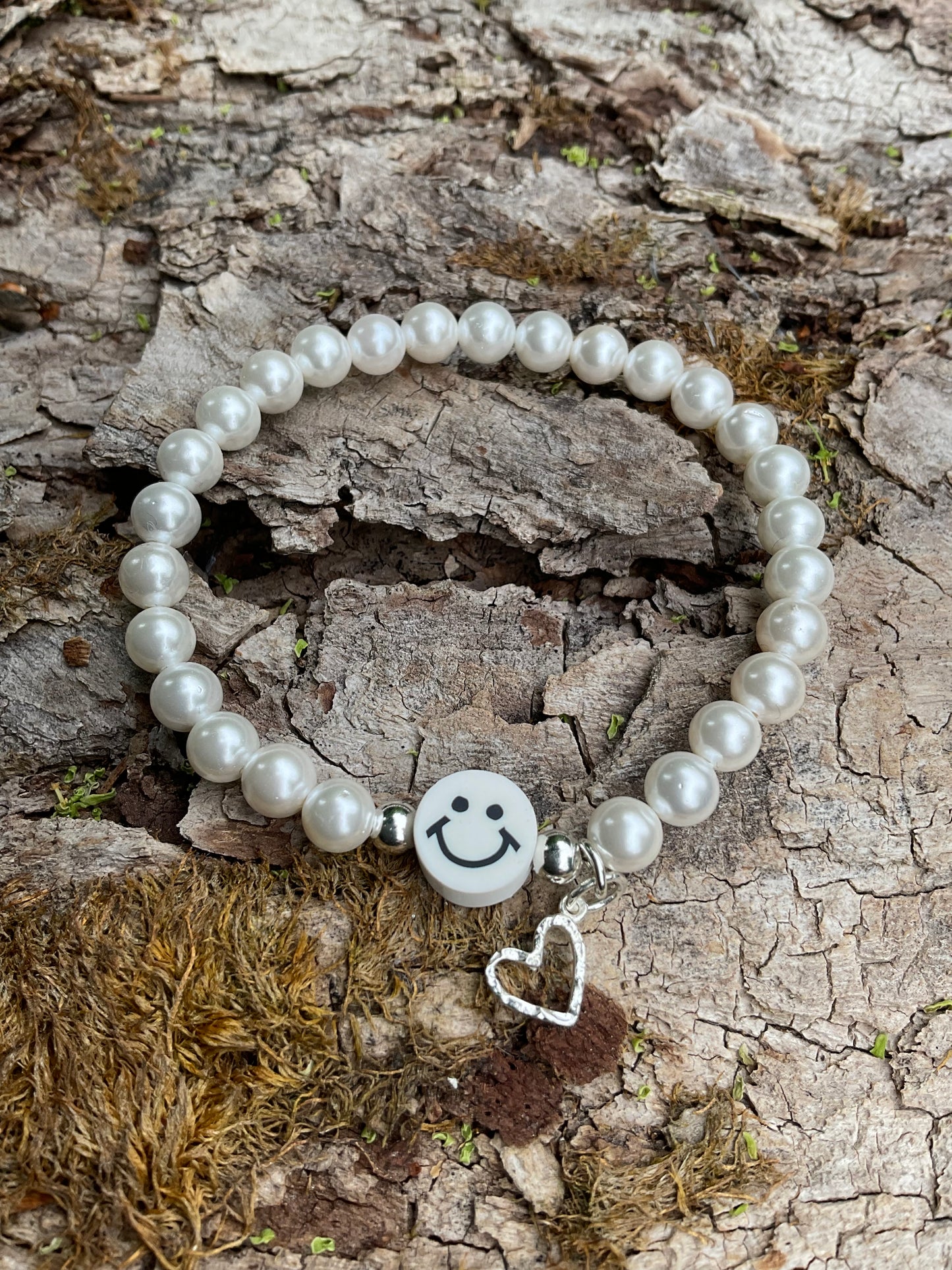 Ein weißes Perlen Armband mit einem weißen Smiley und einem silbernen Herzanhänger
