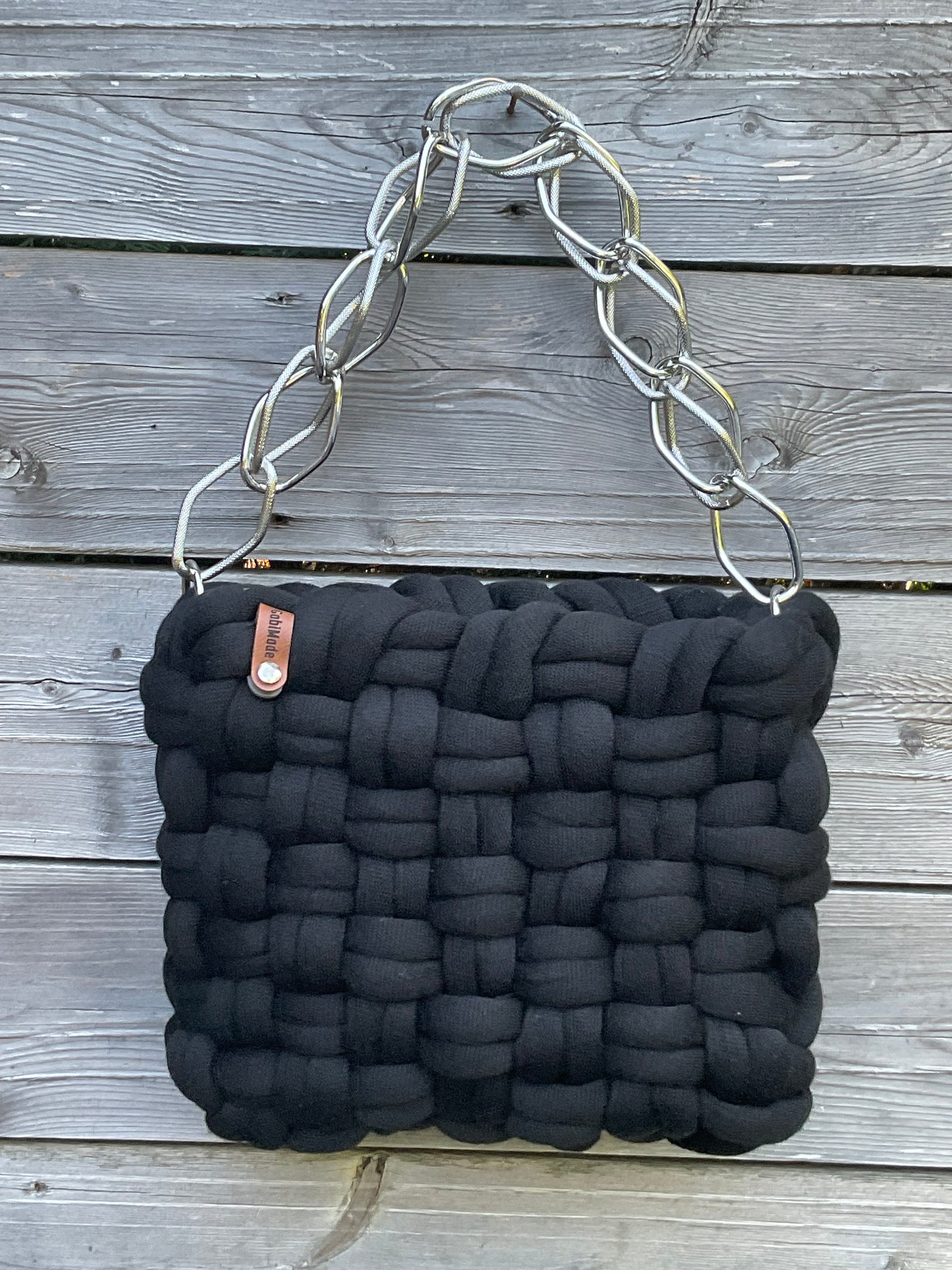 Eine schwarze geflochtene Tasche mit einer Zierkette in Silber