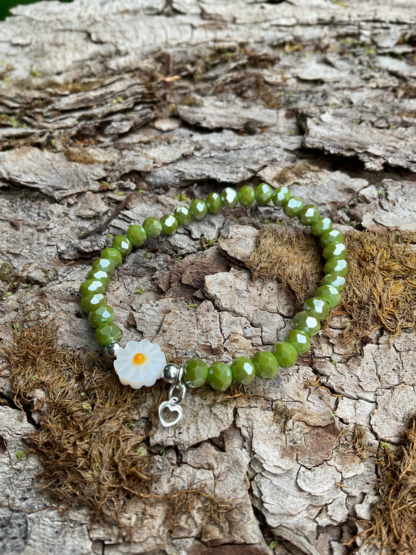 Ein grünes Armband mit einer Blumenperle und einem silbernen Herzanhänger