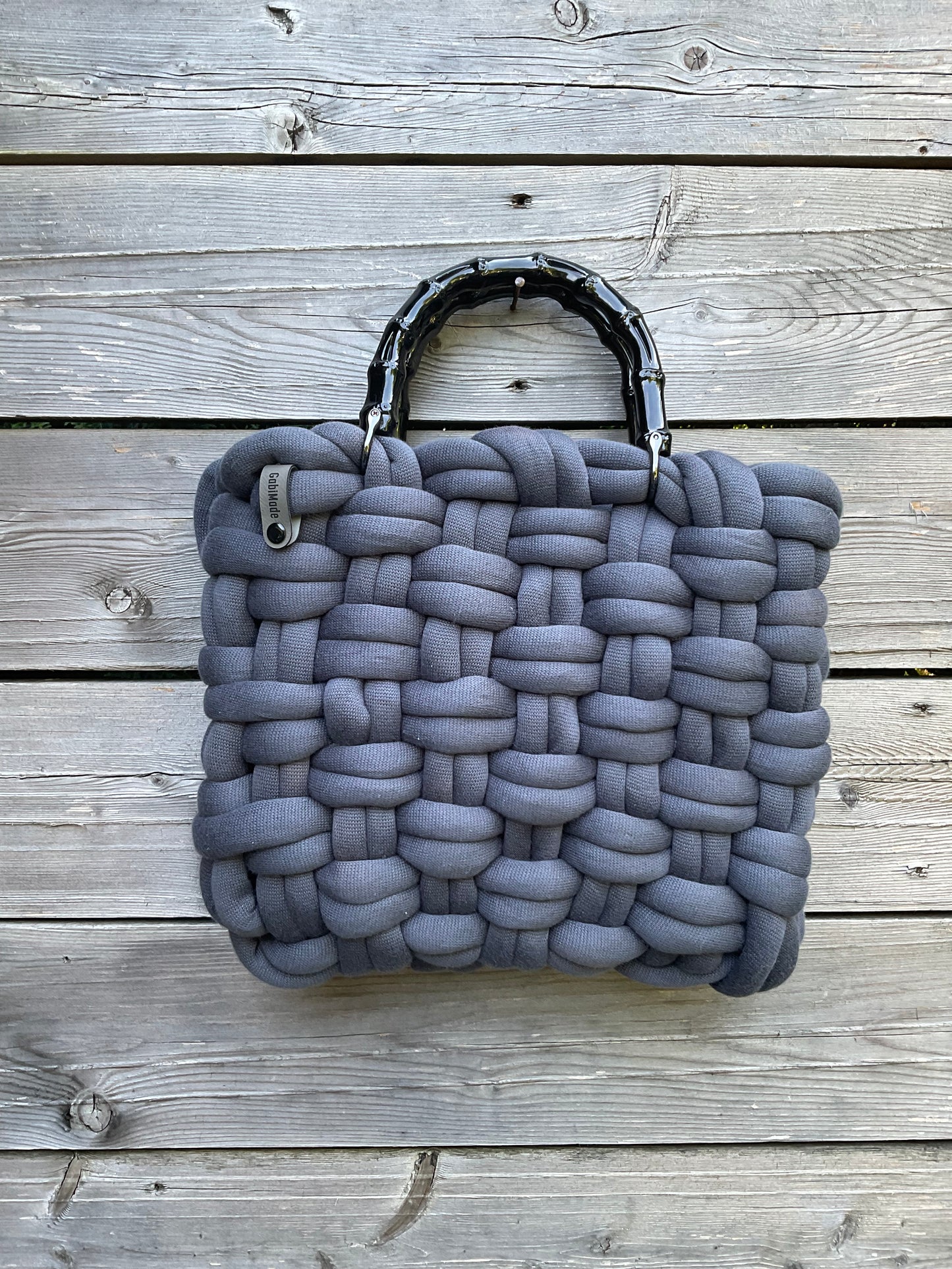 Eine geflochtene Tasche in Grau mit schwarzen Griffen
