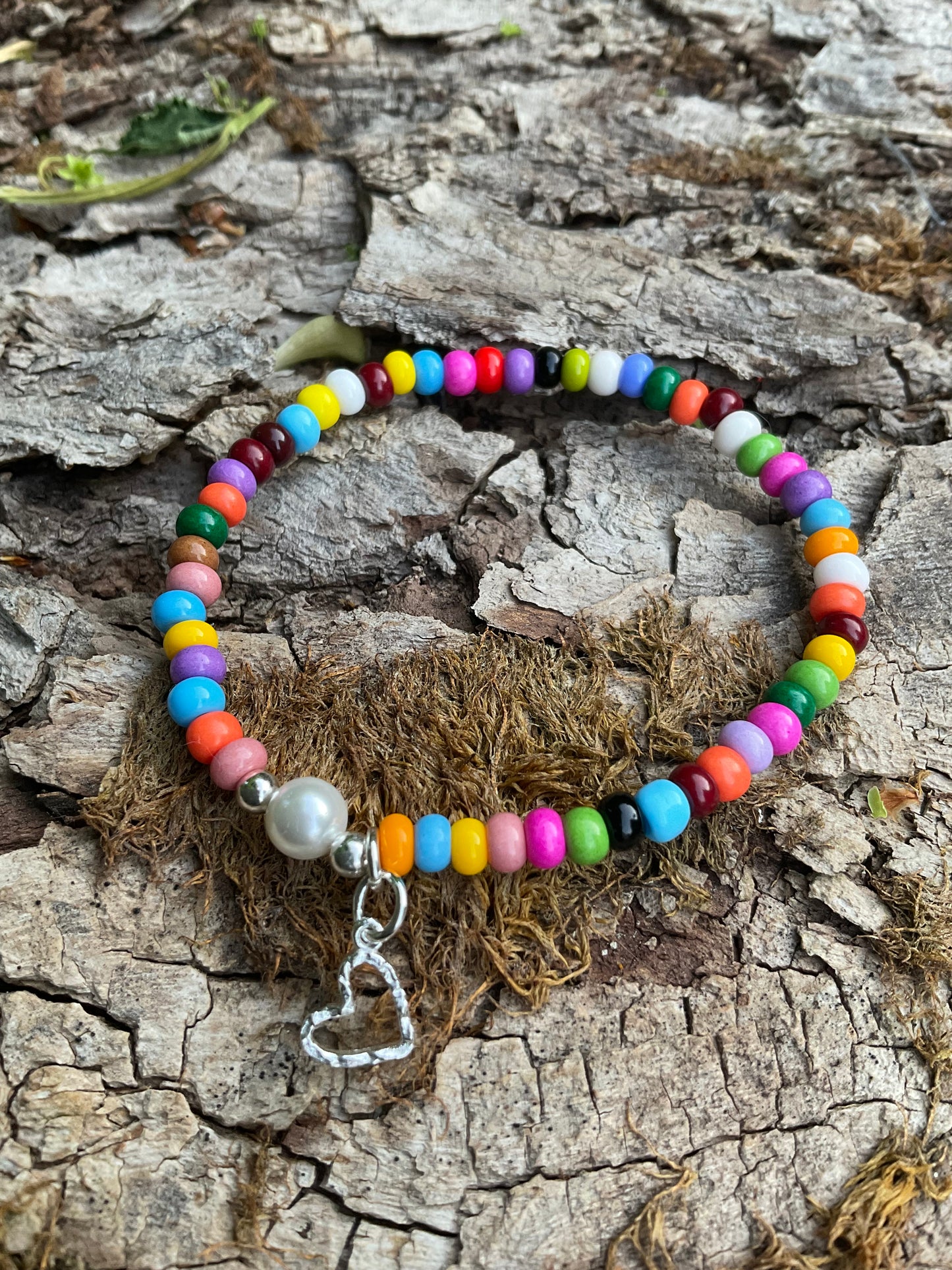 Ein buntes Armband mit einer Perle und einem silbernen Herzanhänger