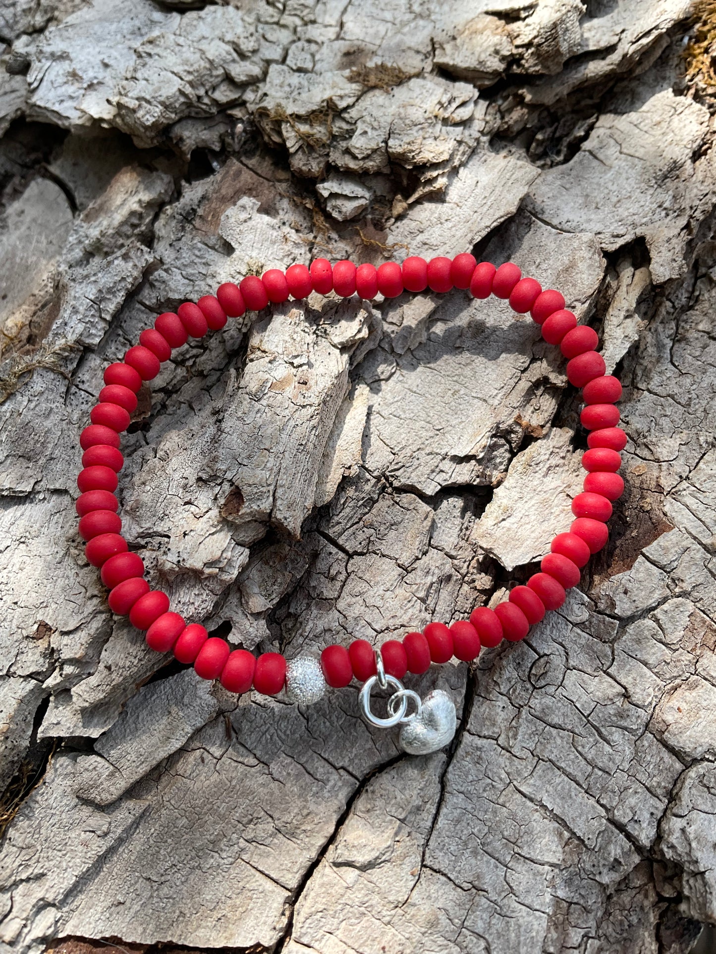 Ein rotes Armband mit einer Glitzerperle und einem Herzanhänger