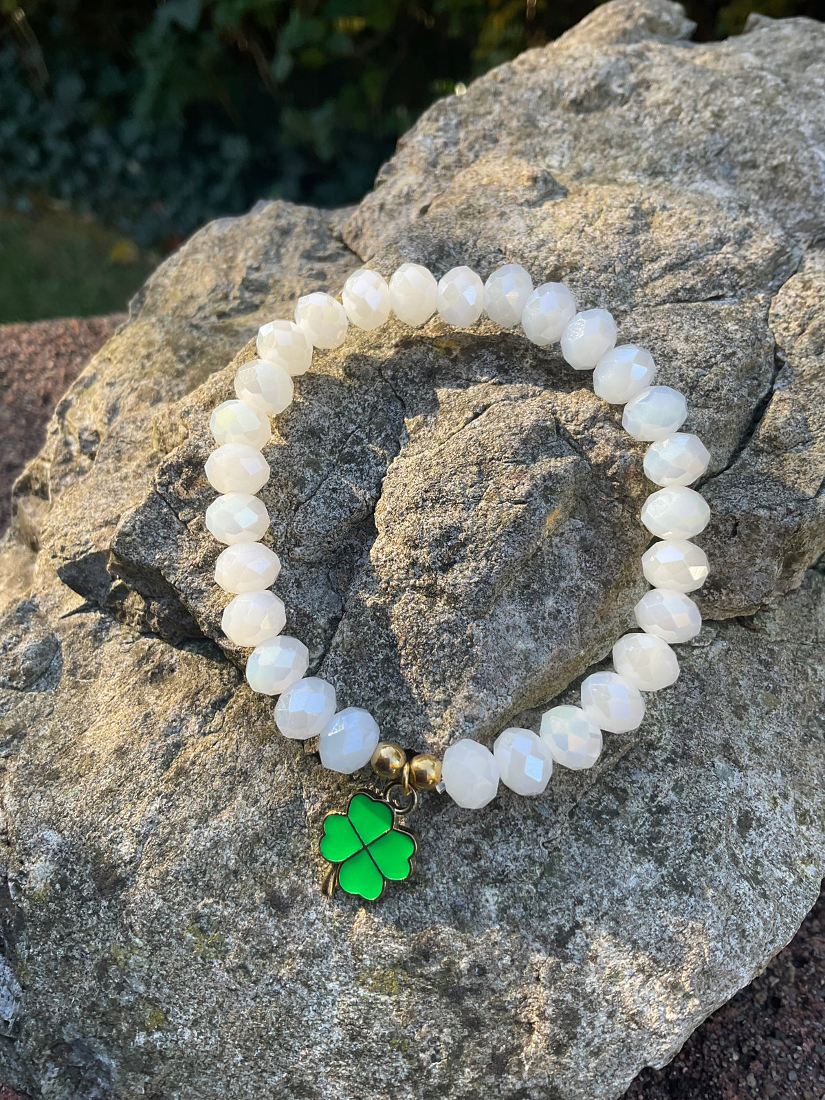 Ein weißes Armband mi emaillierten Klee Anhänger