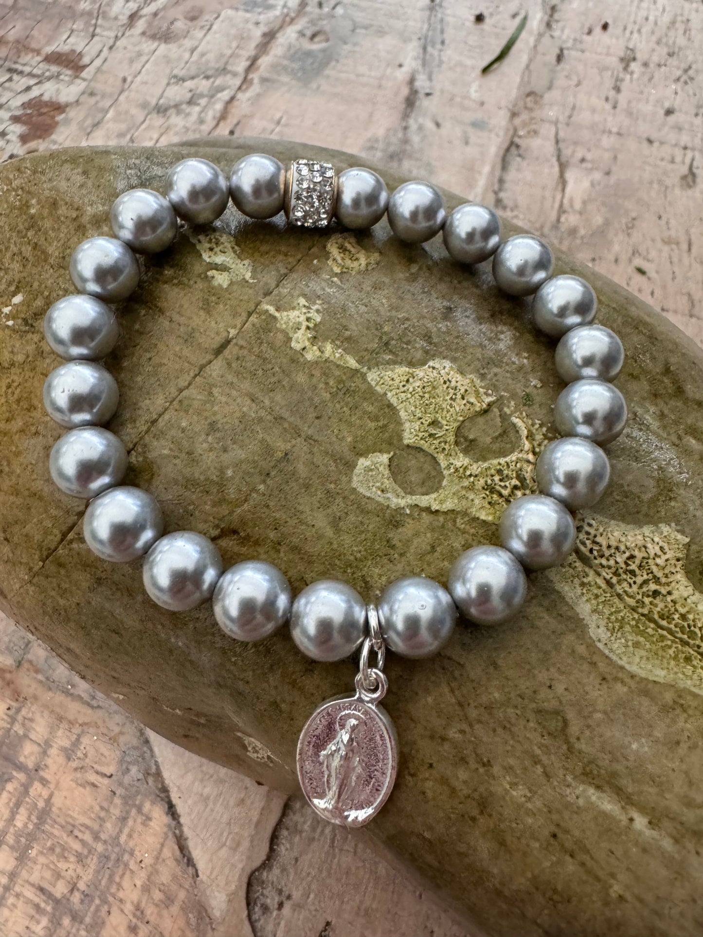Ein graues Perlenarmband mit einem Glitzerrondell und einem silbernen Madonnen Anhänger