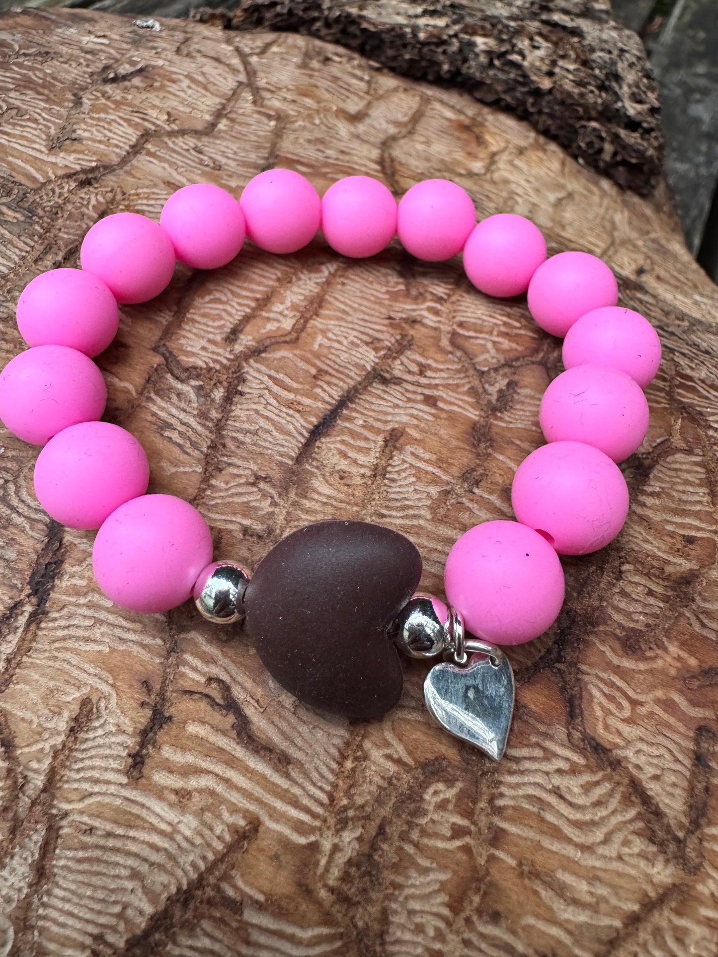 Ein Armband aus pinken Silikonperlen, braunen Silikonherz und Herzanhänger.