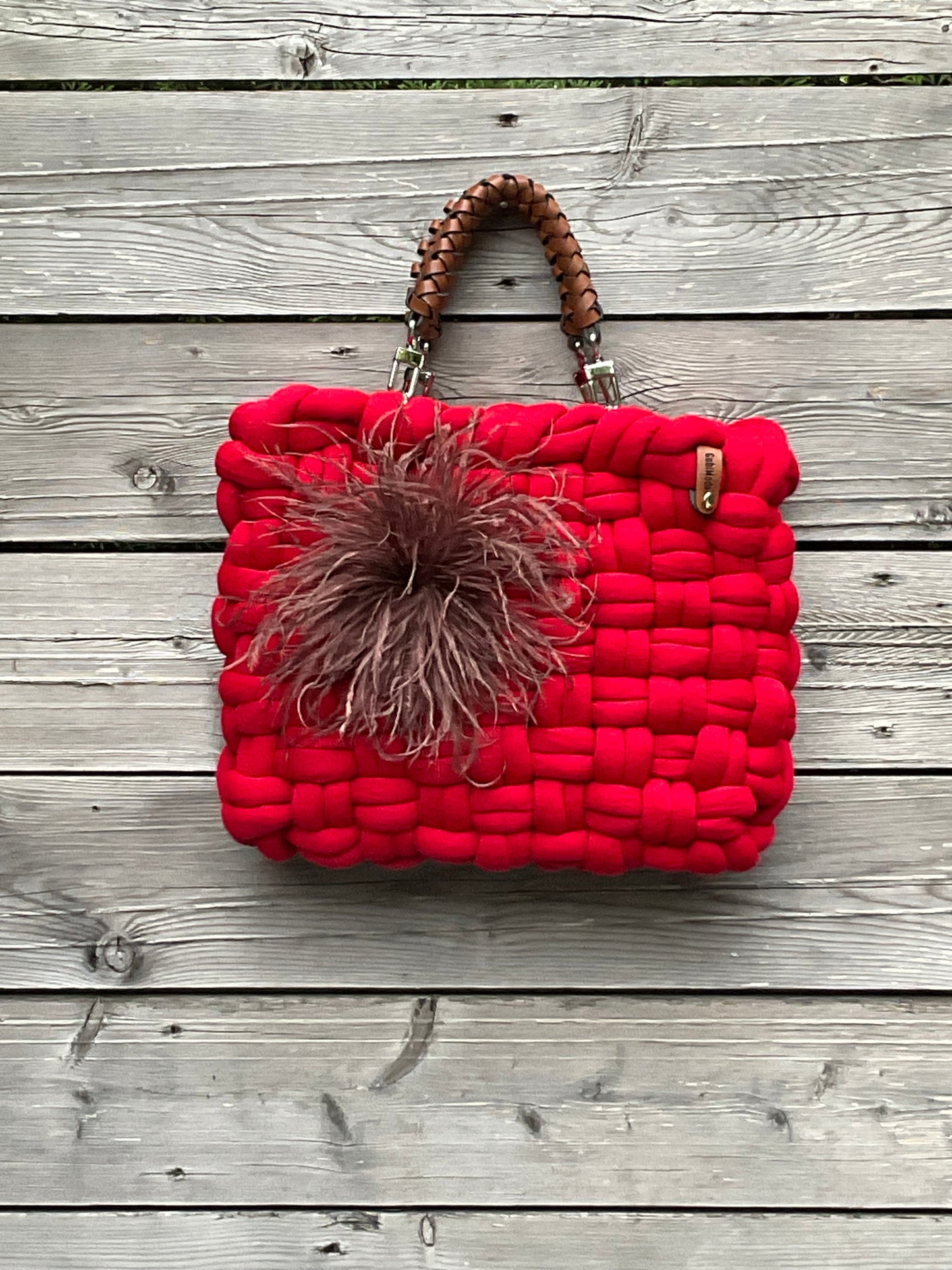 Eine rote gestrickte Tasche mit braunen Ledergriffen und Federbrosche