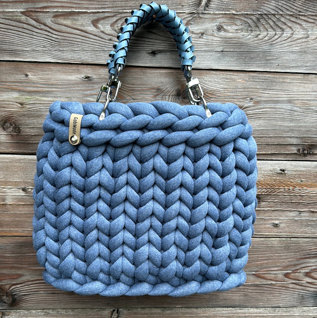 Eine gestrickte Jeansblaue Tasche mit blauen geflochtenen Ledergriffen