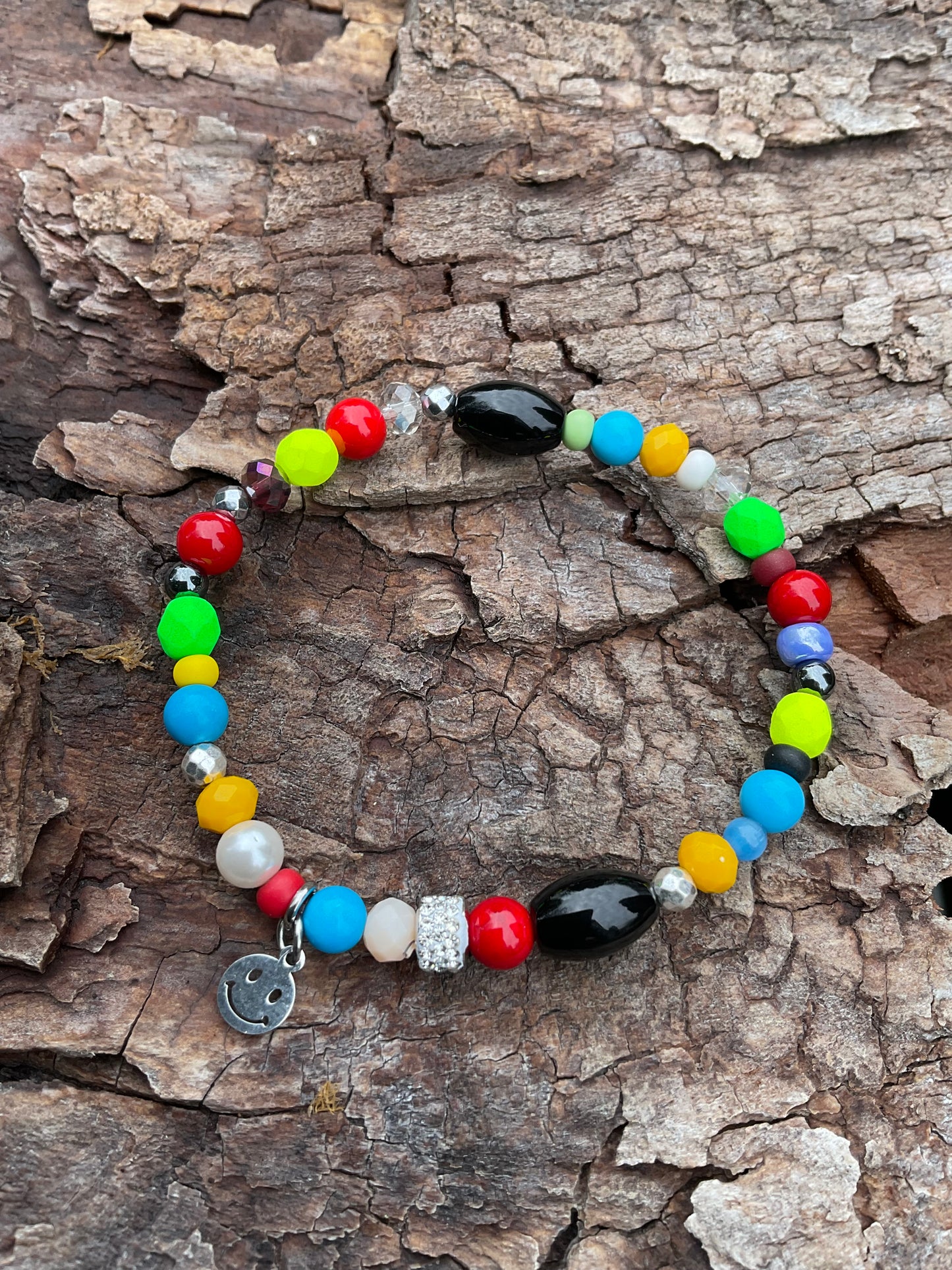 Ein buntes Armband mit einem Glitzerrondell und einem silbernen Smileyanhänger