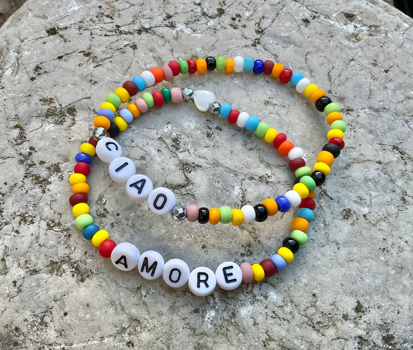 Zwei bunte Armbönder mit dem Worten Ciao und Amore mit einer Herzperle