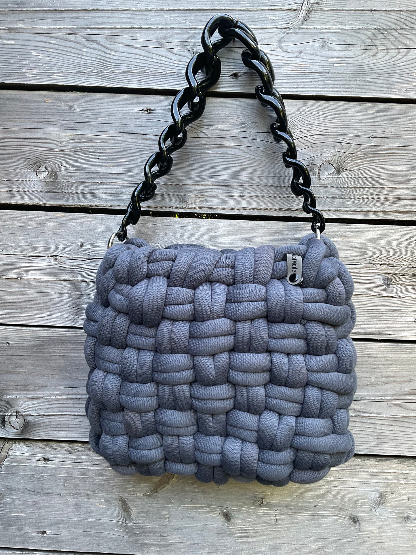 Eine graue geflochtene Tasche mit schwarzer Kunststoff Zierkette
