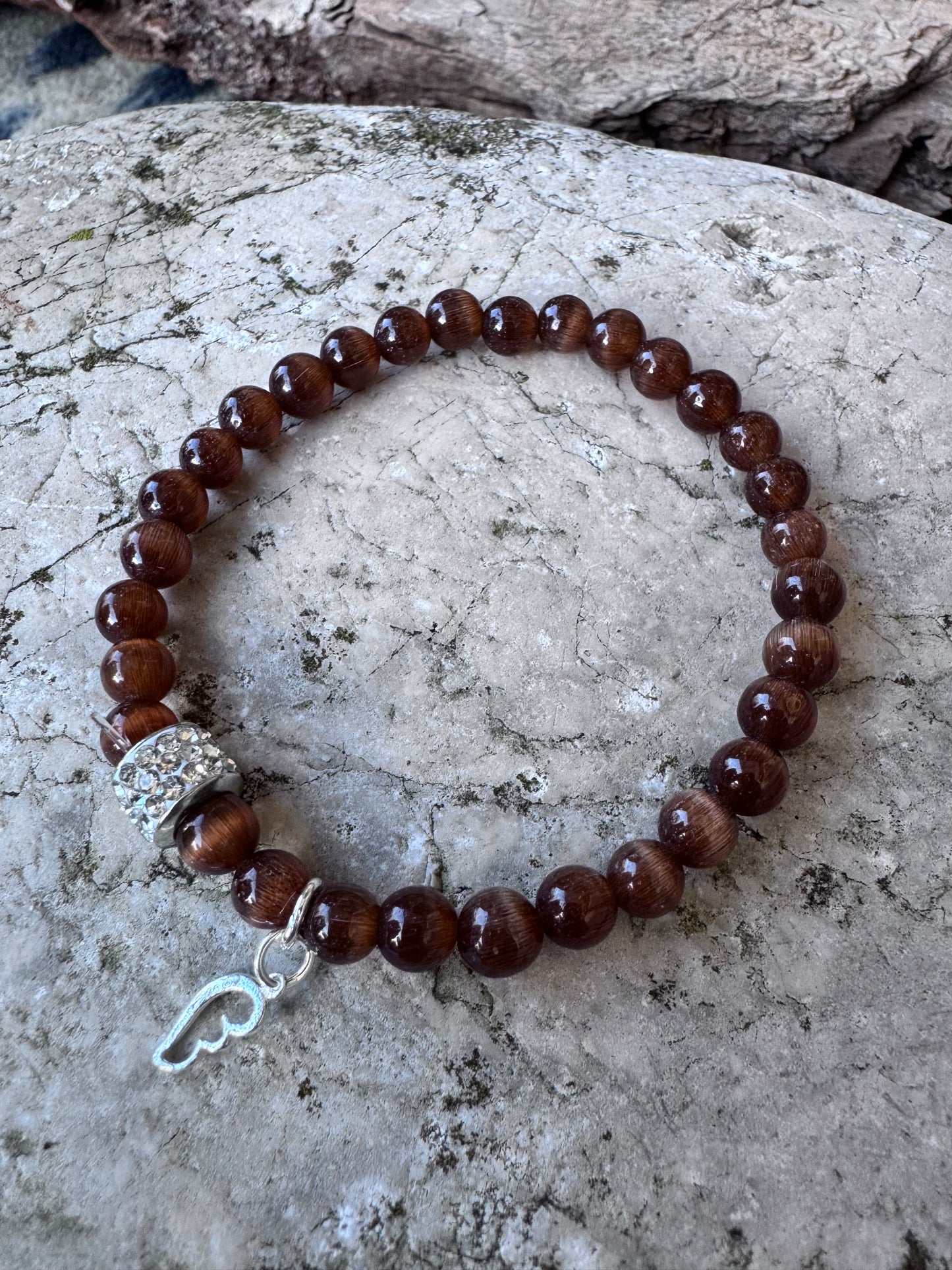 Ein braunes Perlenarmband mit einem Glitzerrondell und einem silbernen Flügelanhänger