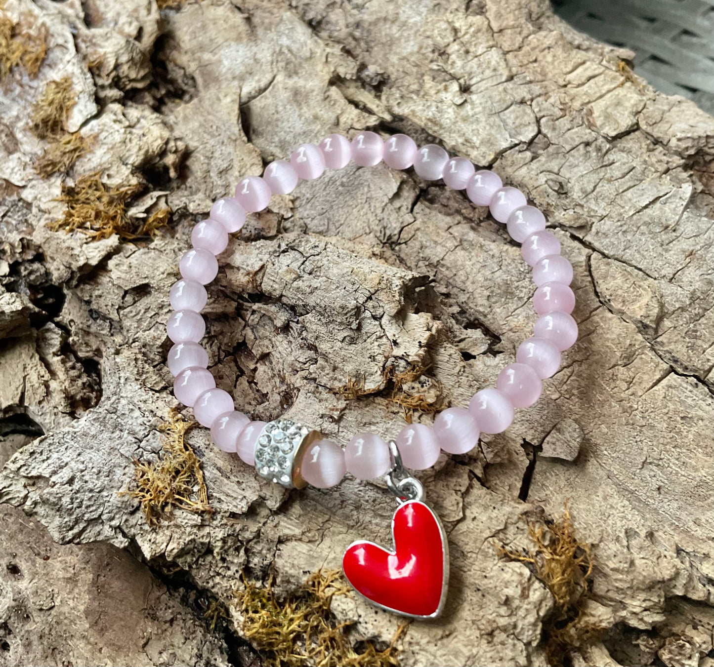 Ein Rosa Perlenarmband mir einem Glitzerrondell und einem roten Herzanhänger