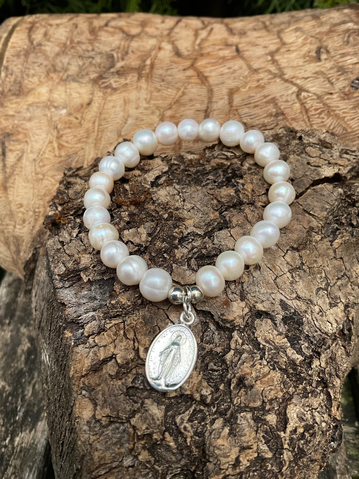 Ein weißes Perlenarmband mit zwei Silberperlen und einem silbernen Madonnen Anhönger