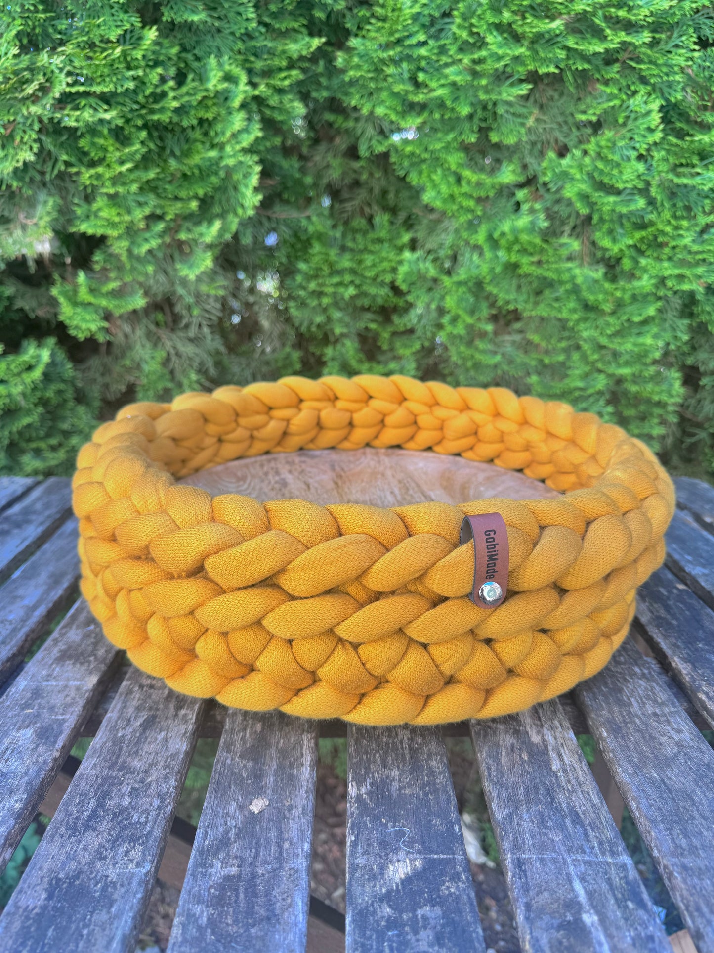 Ein gestricktes Tablett in der Farbe Mango mit Holzteller in Large.
