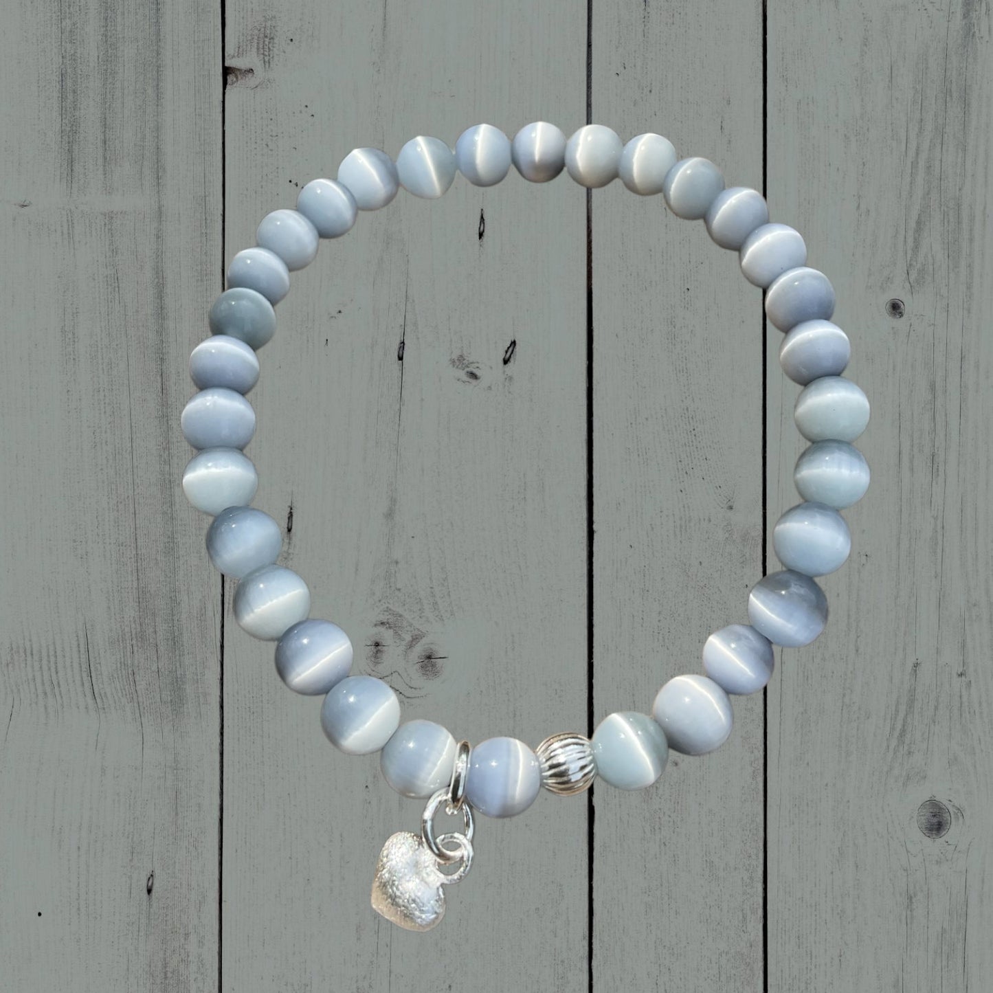 Ein hellgraues Armband mir einer Silberperle und einem silbernen Herzanhänger