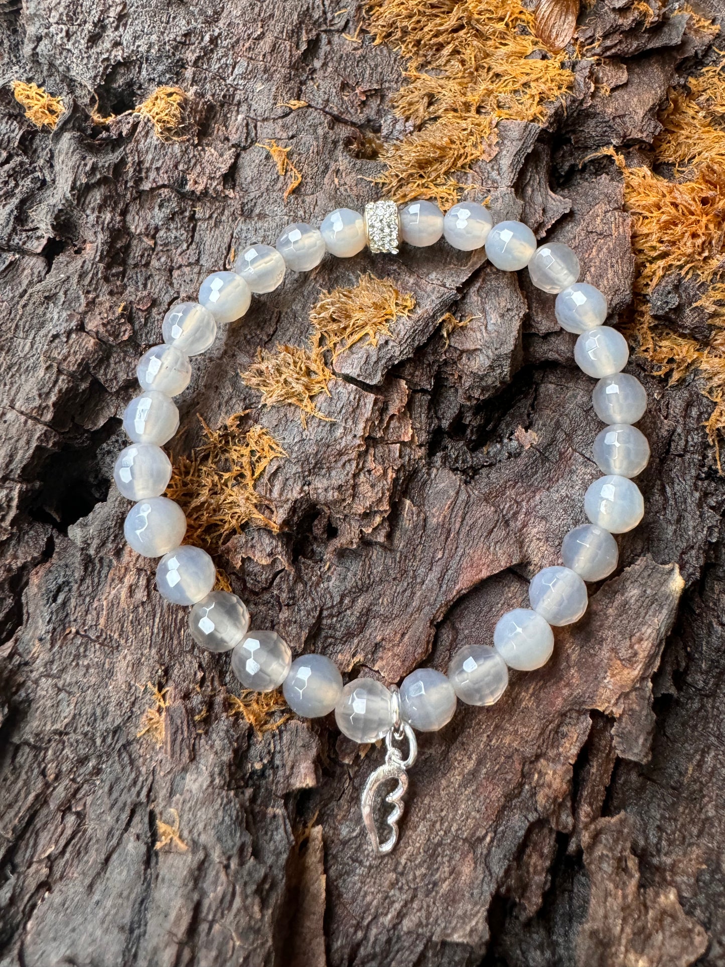 Ein weißes Perlenarmband mit einem Glitzerrondell und einem silbernen Flügel Anhänger