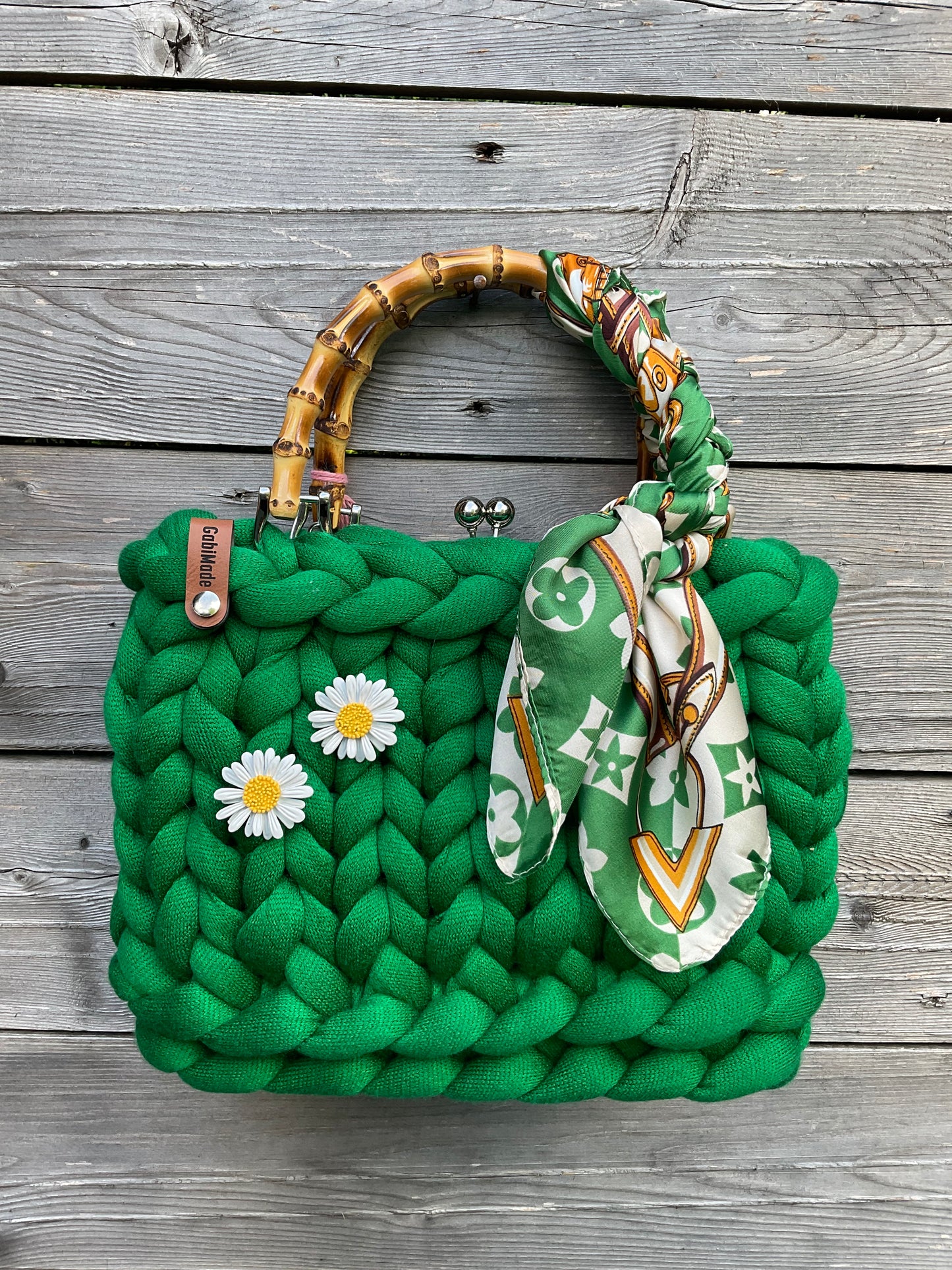 Eine gestrickte grüne Trachtentasche mit einem um den Griff geflochtenen Tuch und zwei Blumenbrochen.