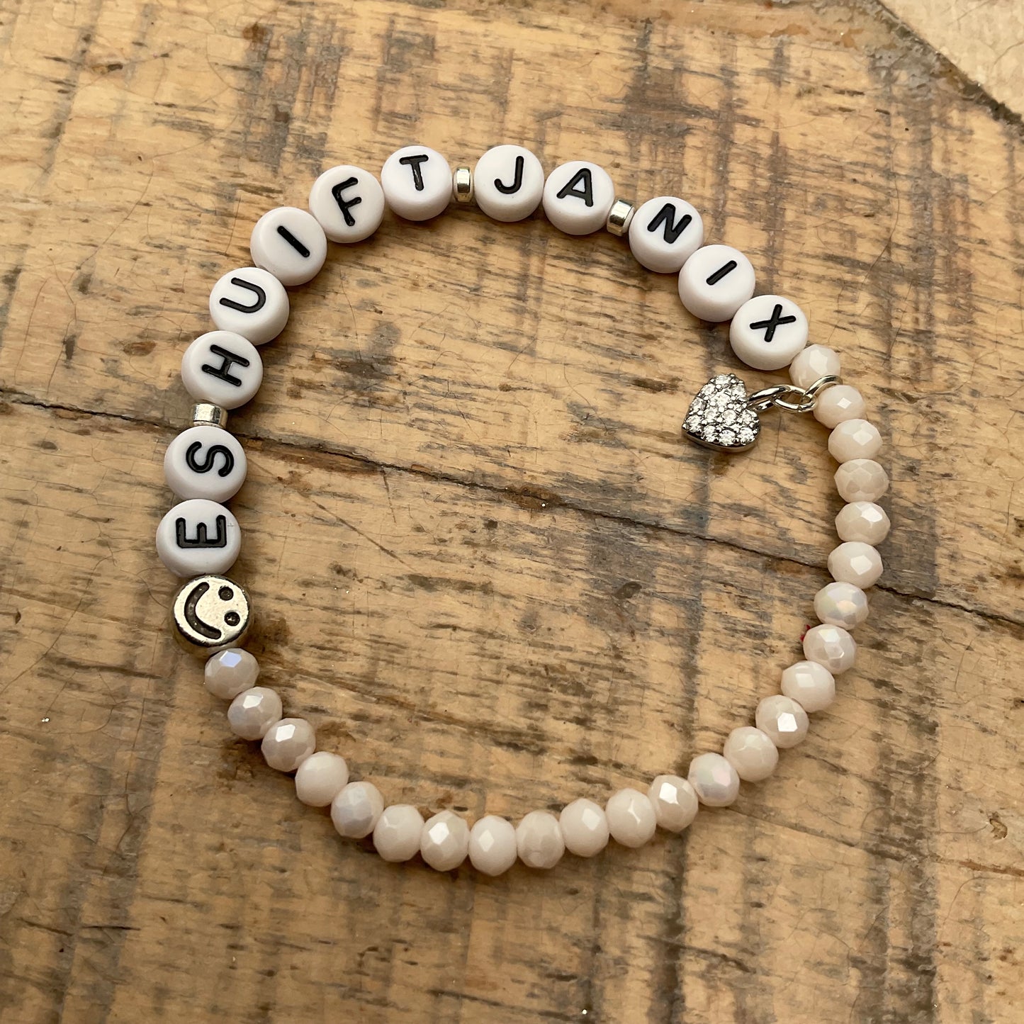 Ein cremefarbenes Perlenarmband mit Schriftzug und Herzanhänger 