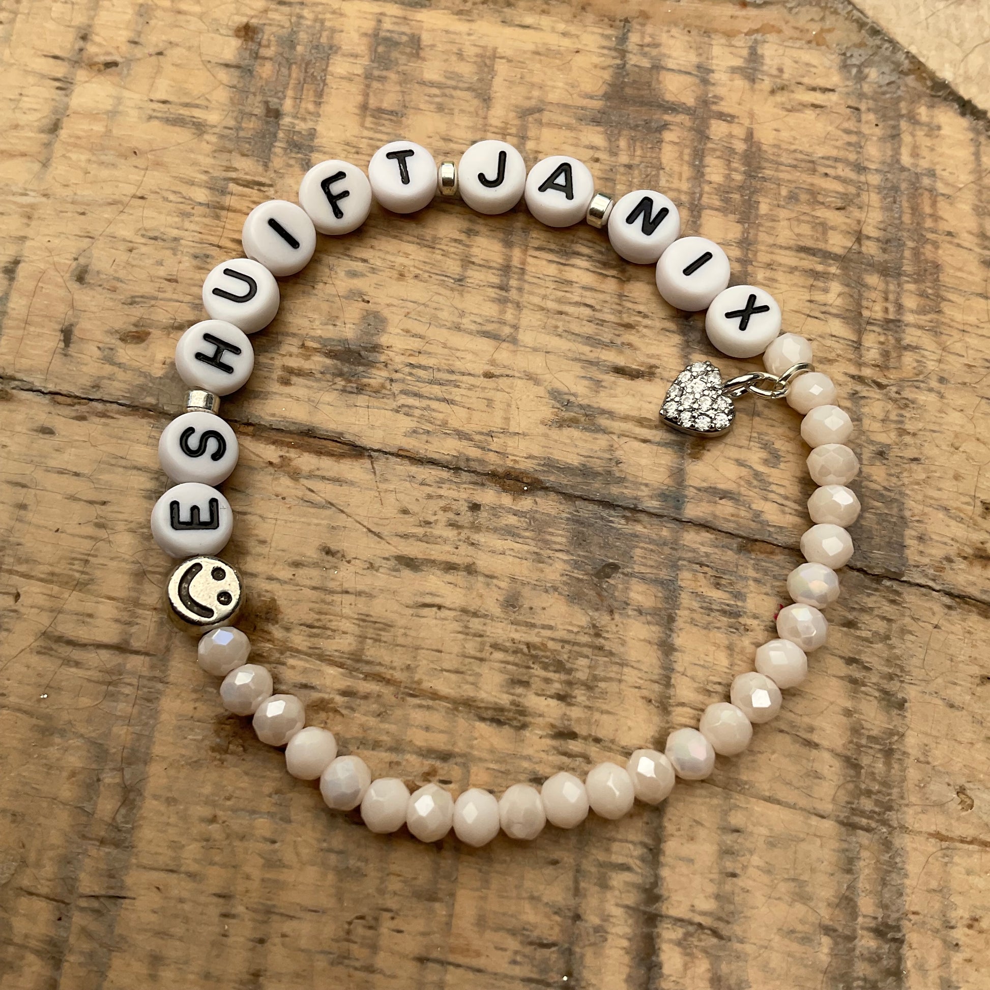 Ein cremefarbenes Perlenarmband mit Schriftzug und Herzanhänger 