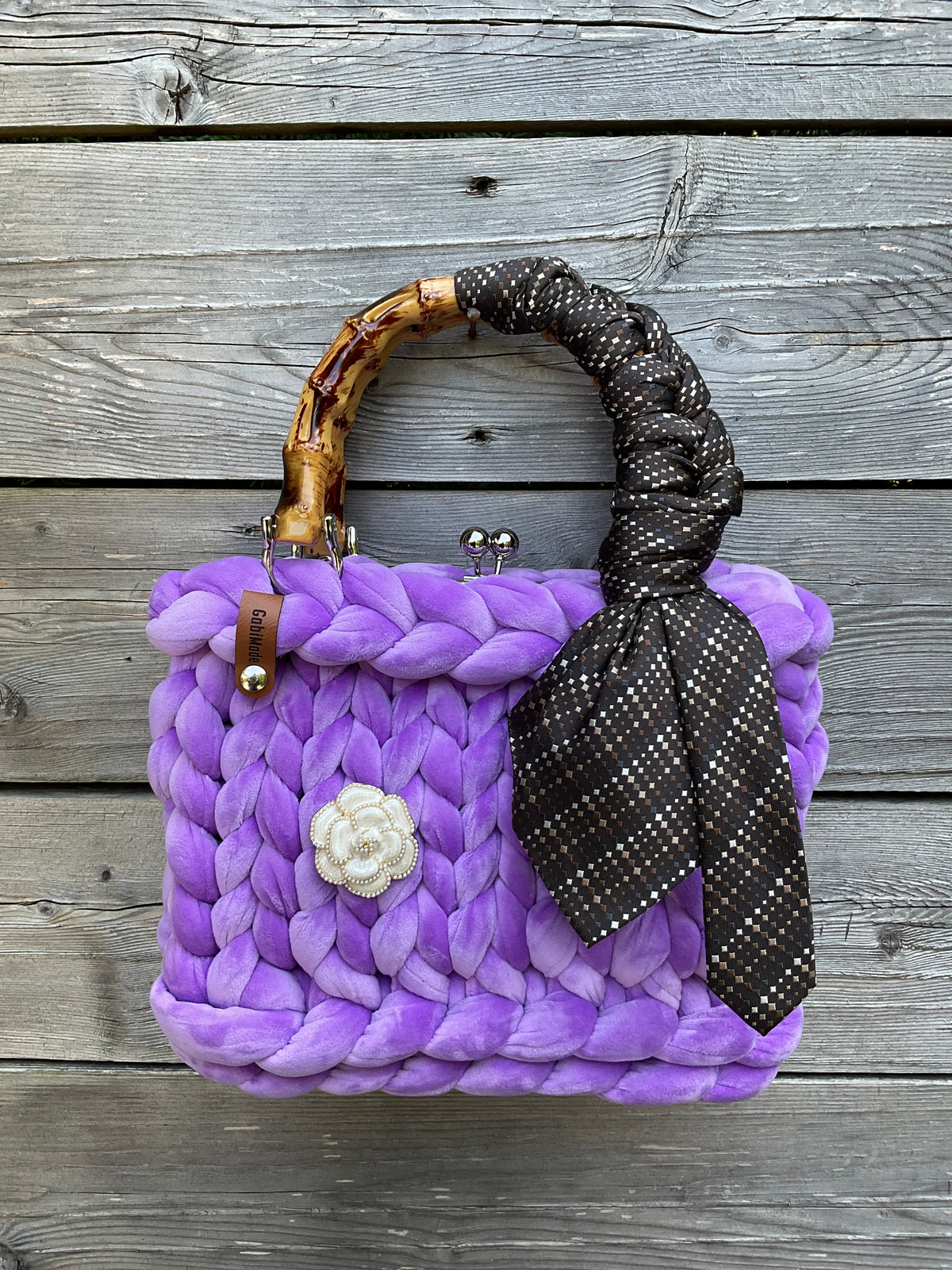 Eine gestrickte lila Trachtentasche mit Brosche und Bambusgriffen 