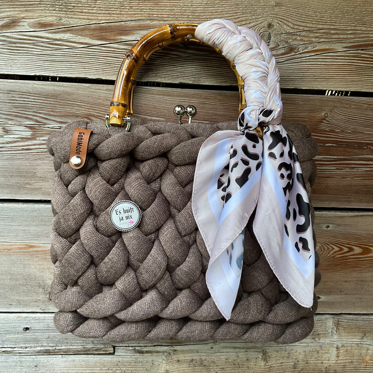 Eine braune gestrickte Trachtentasche mit Gaudiknopf und Bambusgriffen 