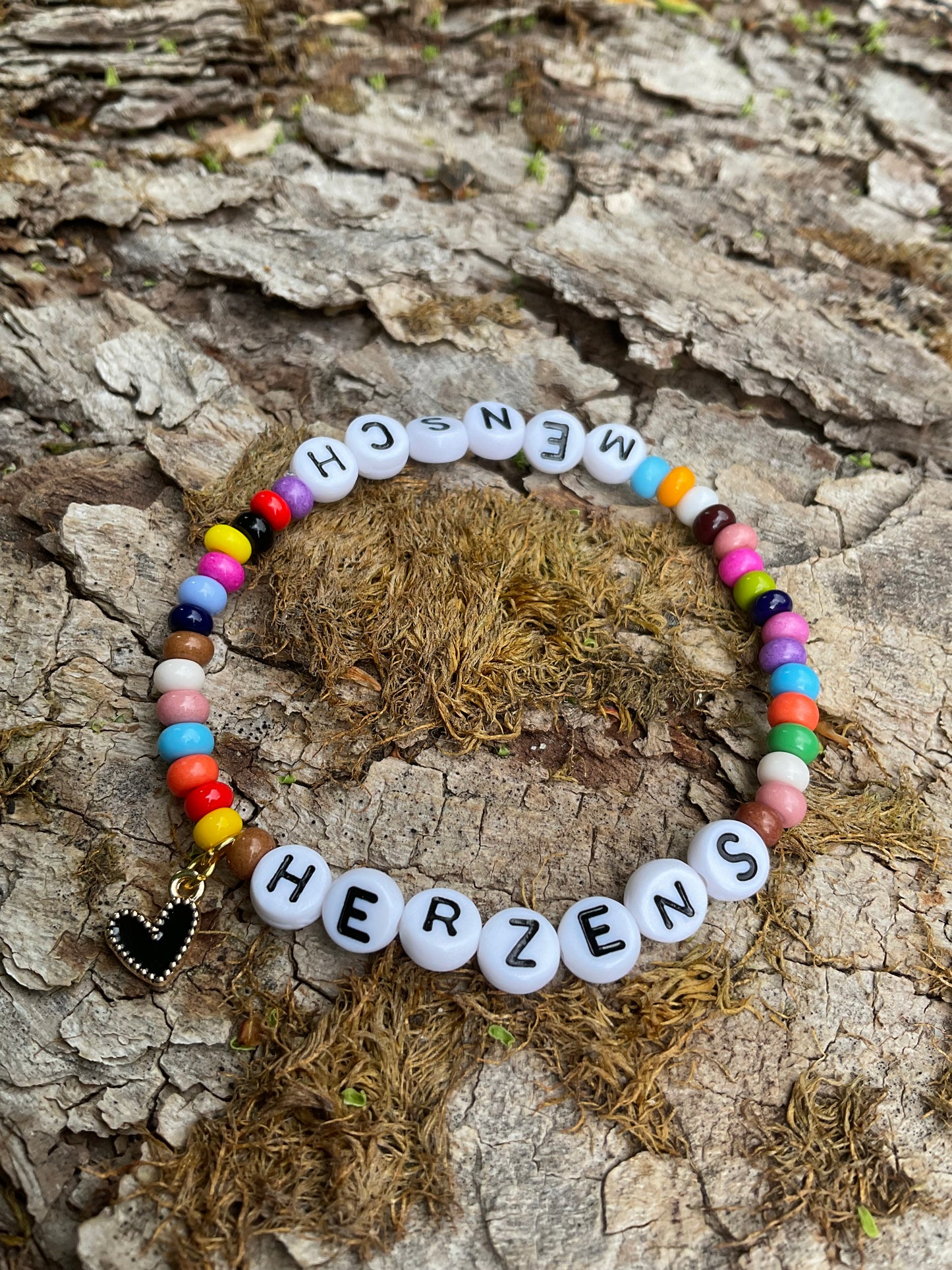 Ein Armband aus bunten Perlen mit dem Wort Herzensmensch und einem schwarzen Herzanhänger
