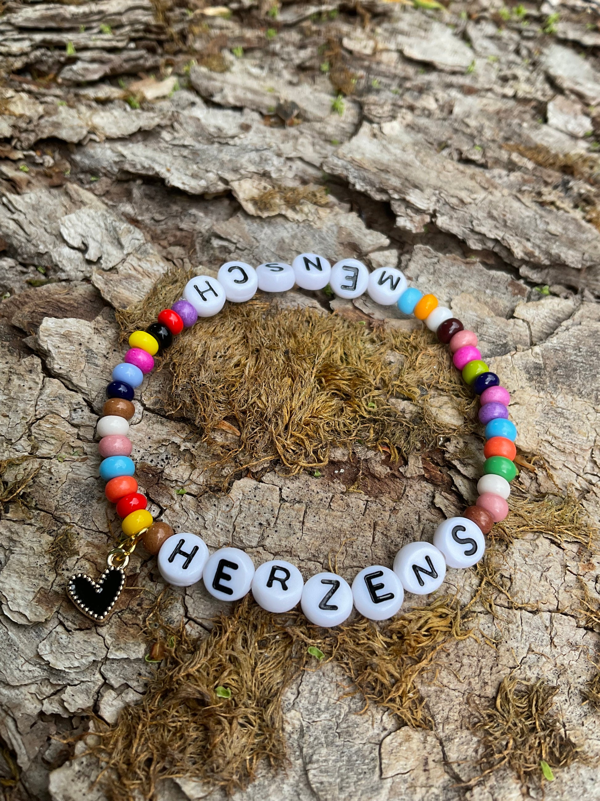 Ein Armband aus bunten Perlen mit dem Wort Herzensmensch und einem schwarzen Herzanhänger