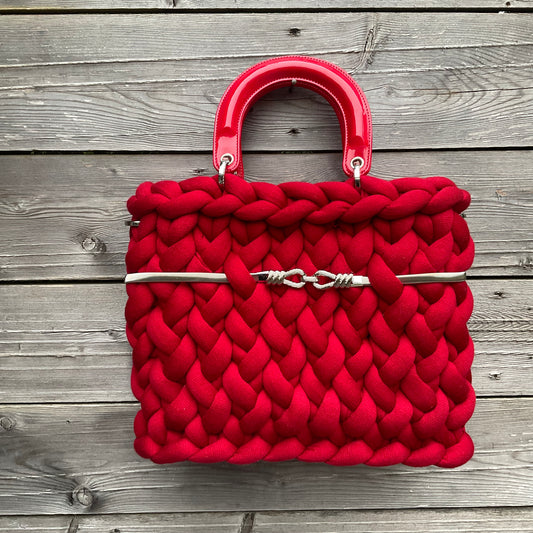 Eine gestrickte rote Tasche mit Gurt und Henkeln 