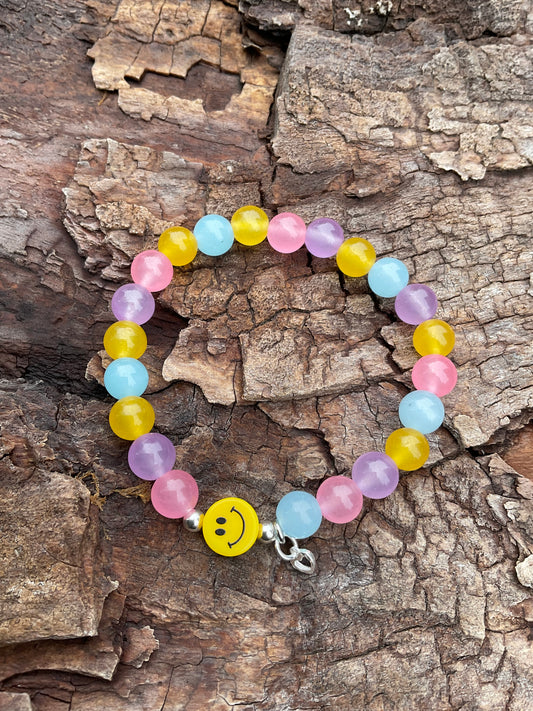 Ein buntes Armband mit einer gelben Smileyperle und einem silbernen Herzanhänger