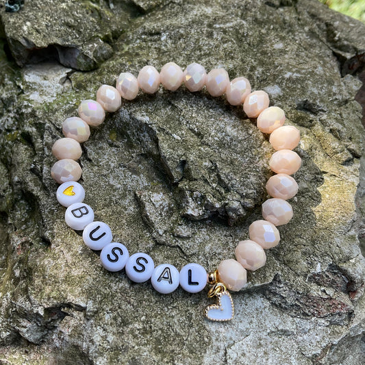 Ein cremefarbenes Perlenarmband mit Bussal und Herzanhänger 