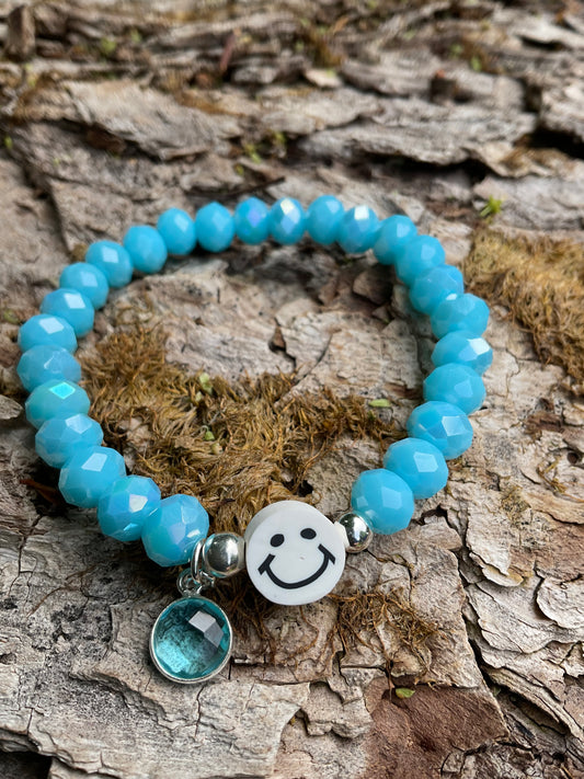 Ein blaues Armband mit einem weißen Smiley und einem blauen Anhänger 