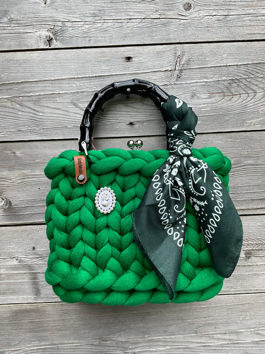 Eine grüne gestrickte Trachtentaschen mit schwarzen Griffen