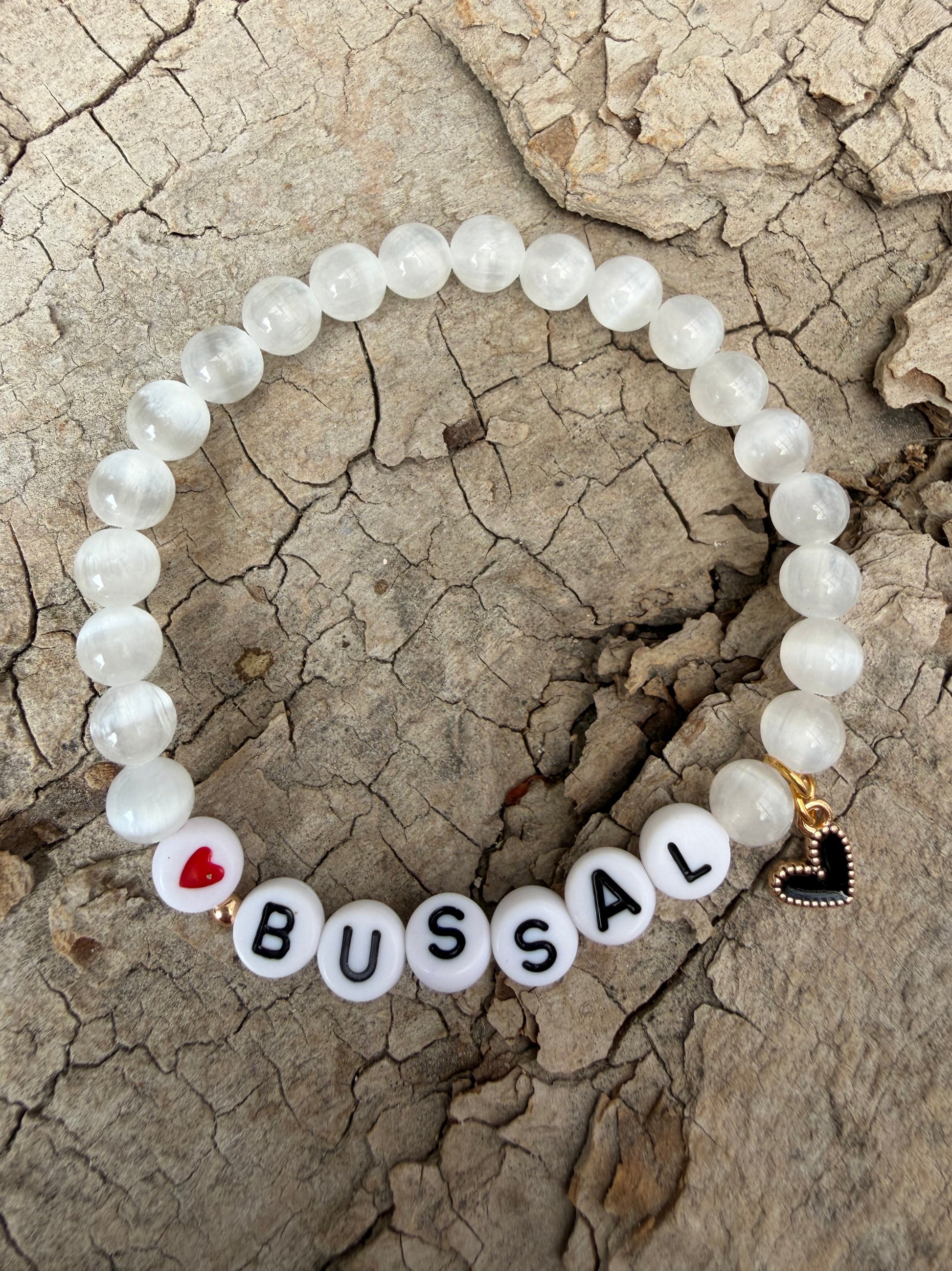 Ein weißes perlenarmband mit Bussal und Herzanhänger 