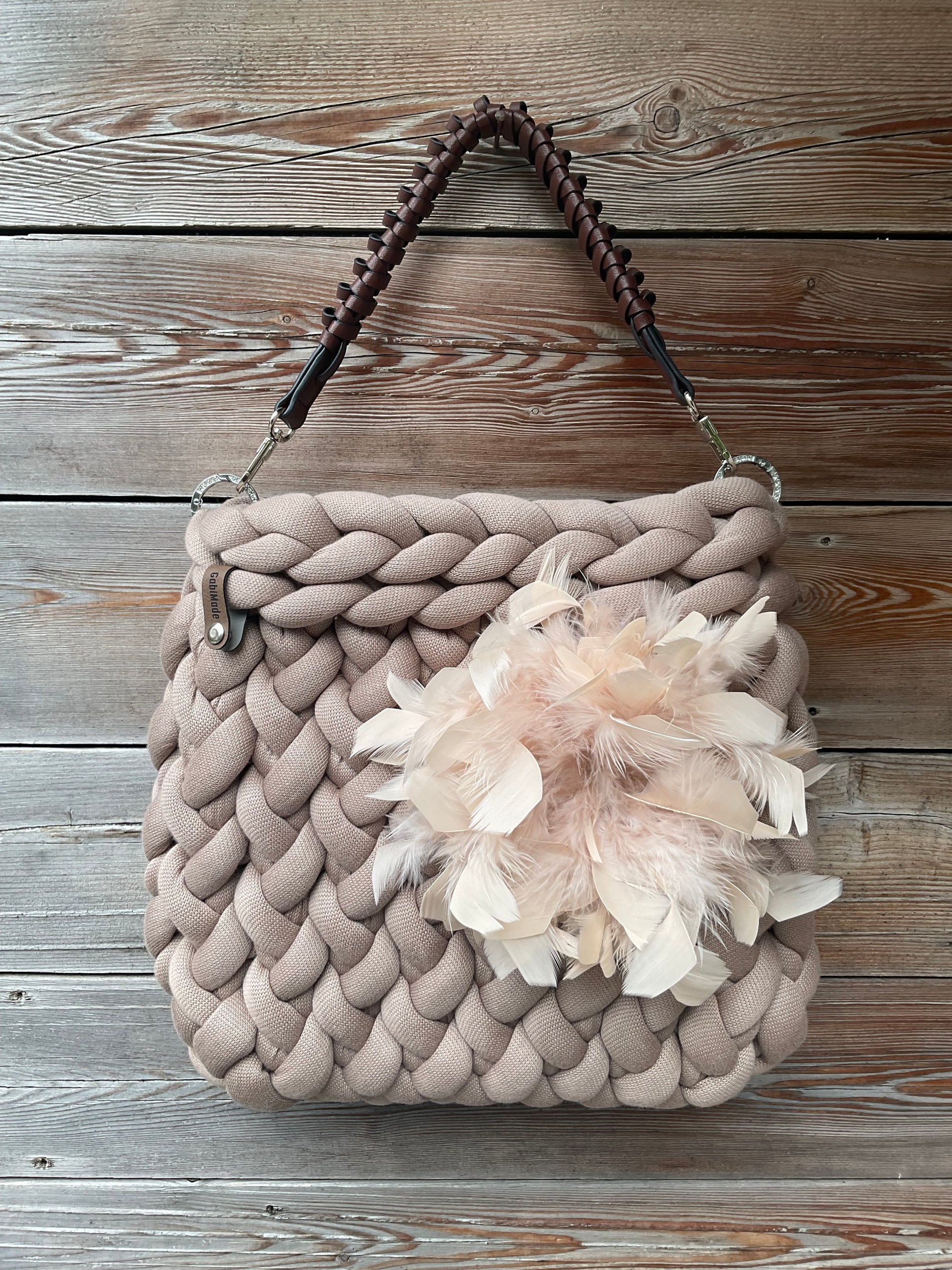 Eine gestrickte beige Tasche mit Federbrosche und Griff 