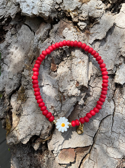 Ein rotes Armband mit einer weißen  Blumenperle und einem goldenen Herzanhänger