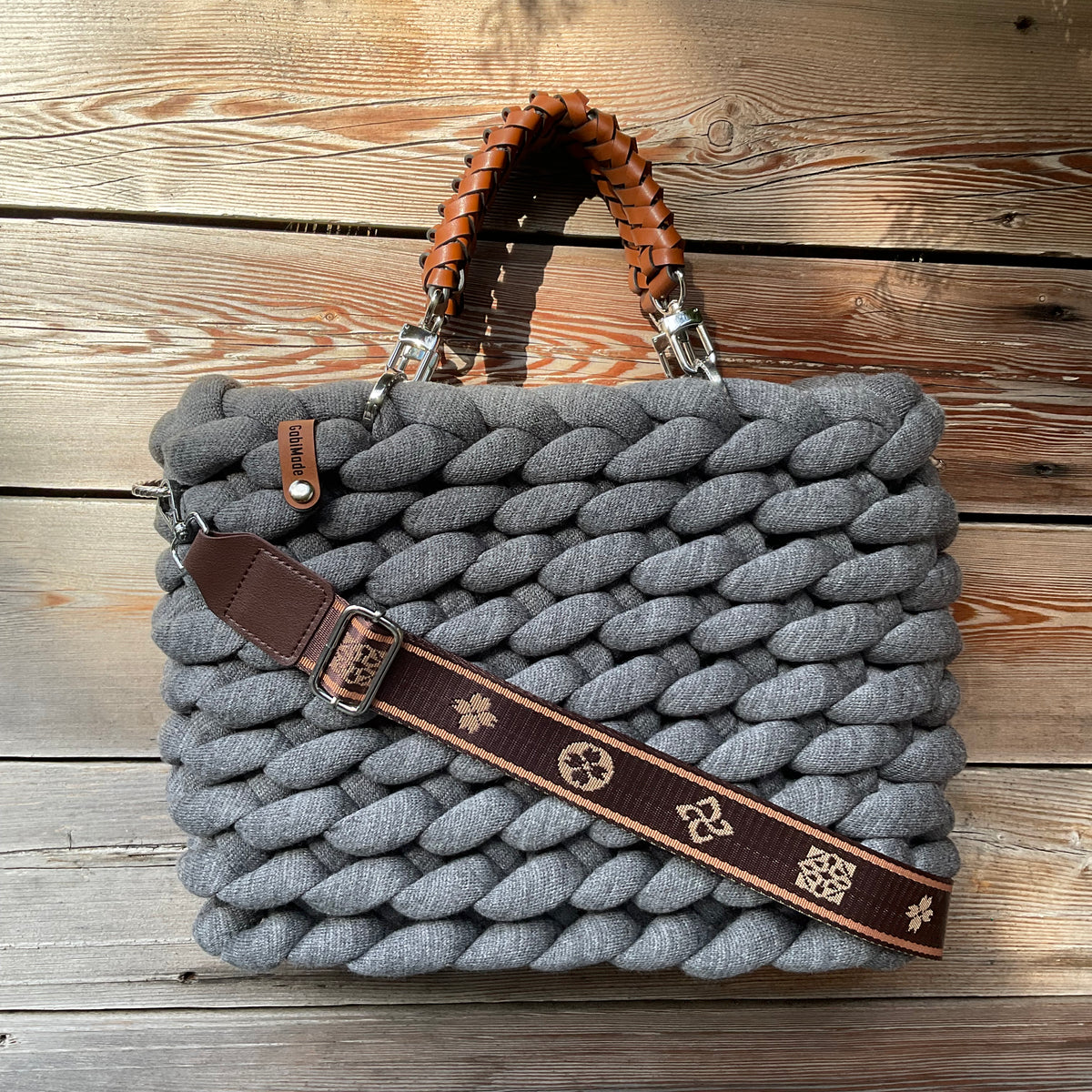 Eine gestrickte graue Tasche mit braunen Griffen und Gurt 