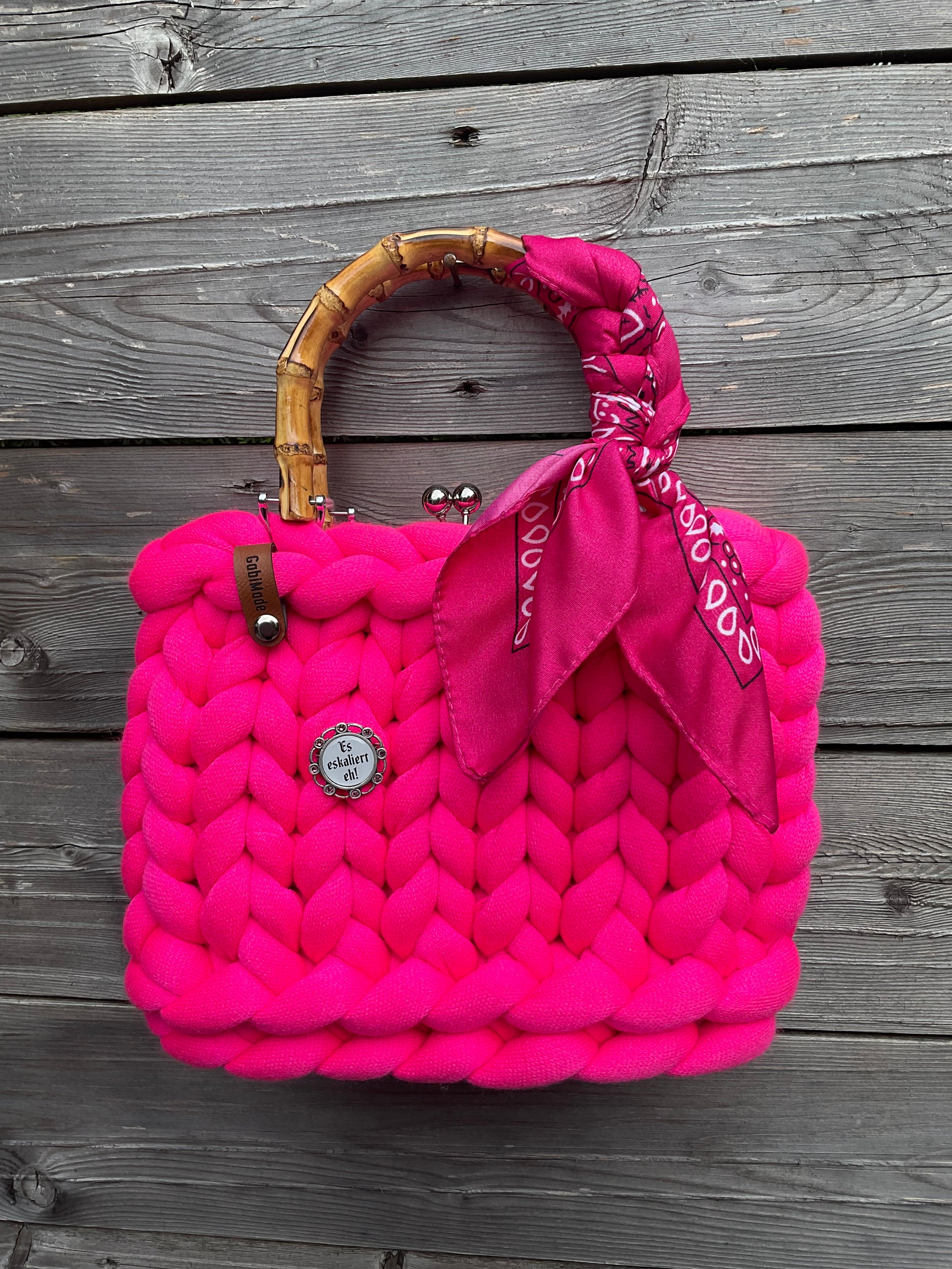 Eine gestrickte pinke Trachtentasche mi einem um den Griff geknotetem Tuch und einer Brosche.