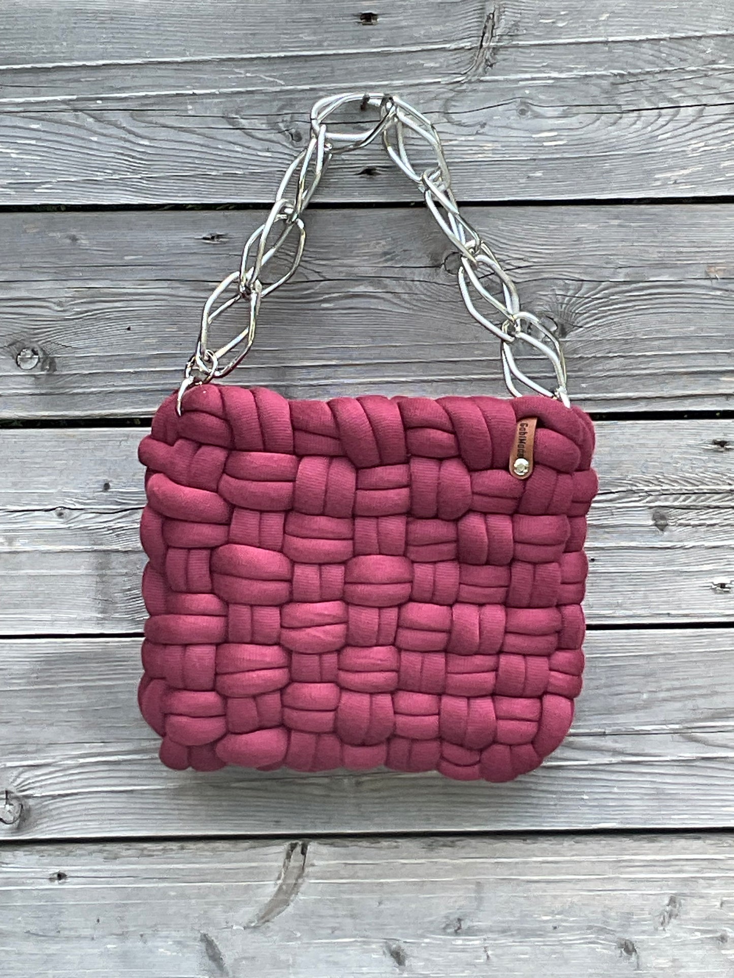 Eine Bordeauxrot geflochtene Tasche mit silberner Kette 