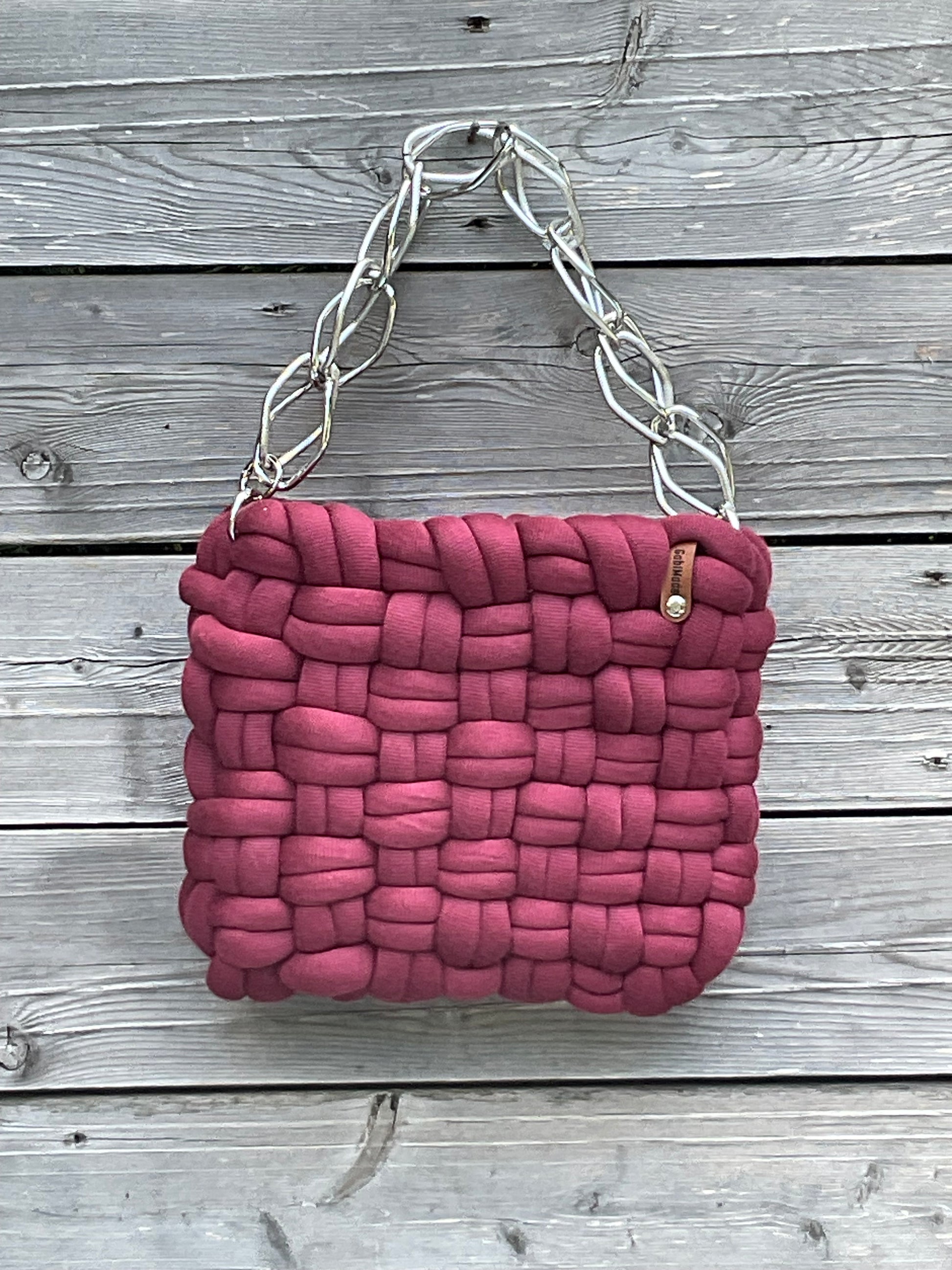 Eine Bordeauxrot geflochtene Tasche mit silberner Kette 