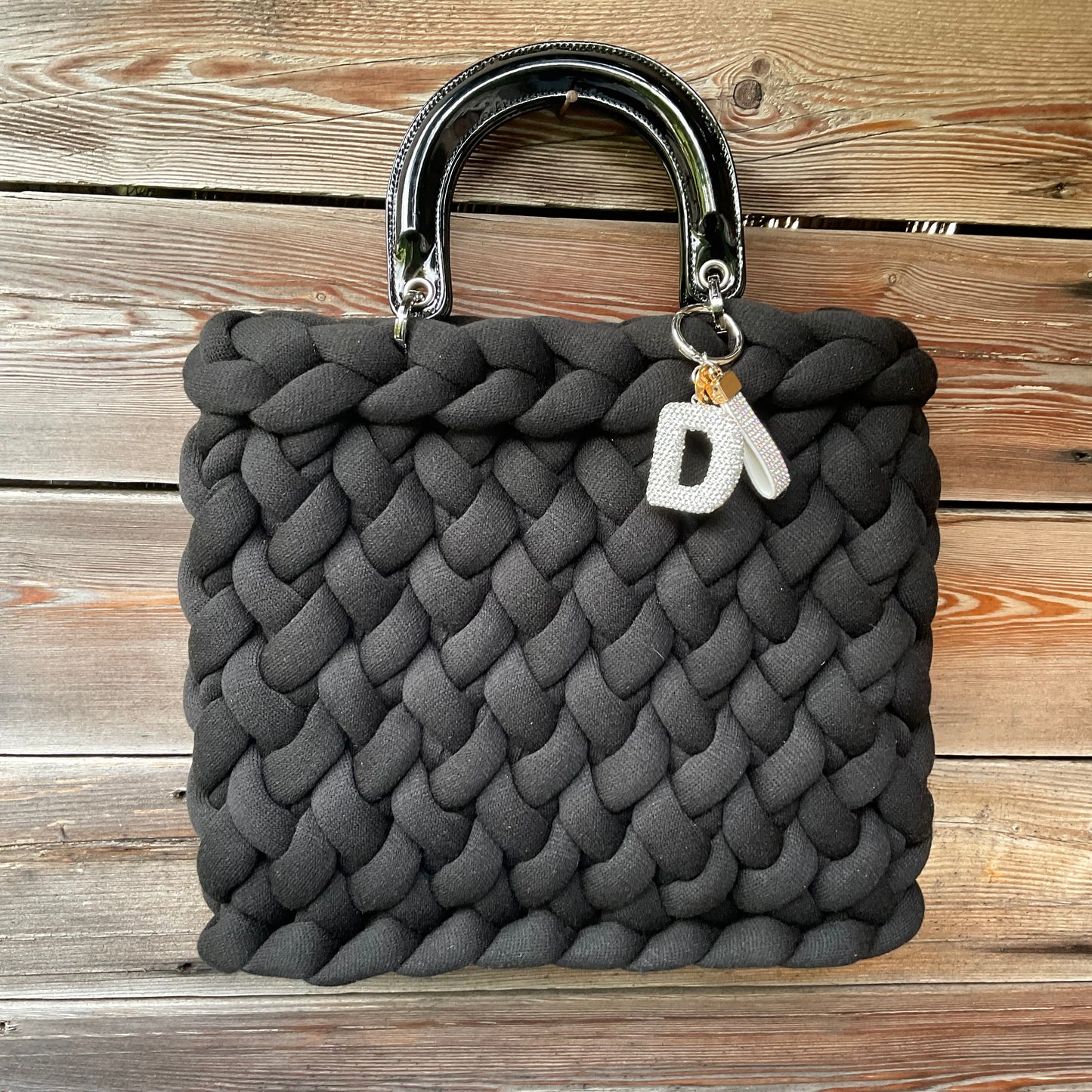 Eine gestrickte schware Tasche mit Anhänger und Lackhenkel