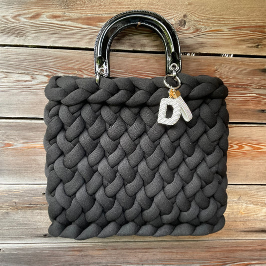 Eine gestrickte schware Tasche mit Anhänger und Lackhenkel