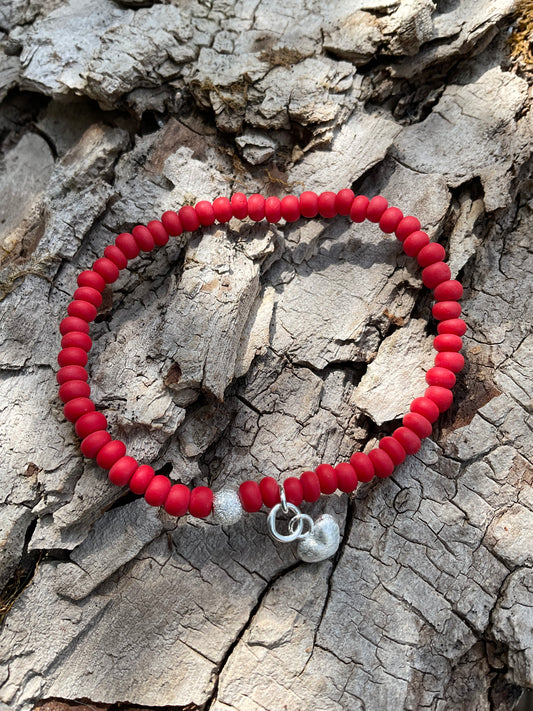 Ein rotes Armband mit einer Glitzerperle und einem Herzanhänger