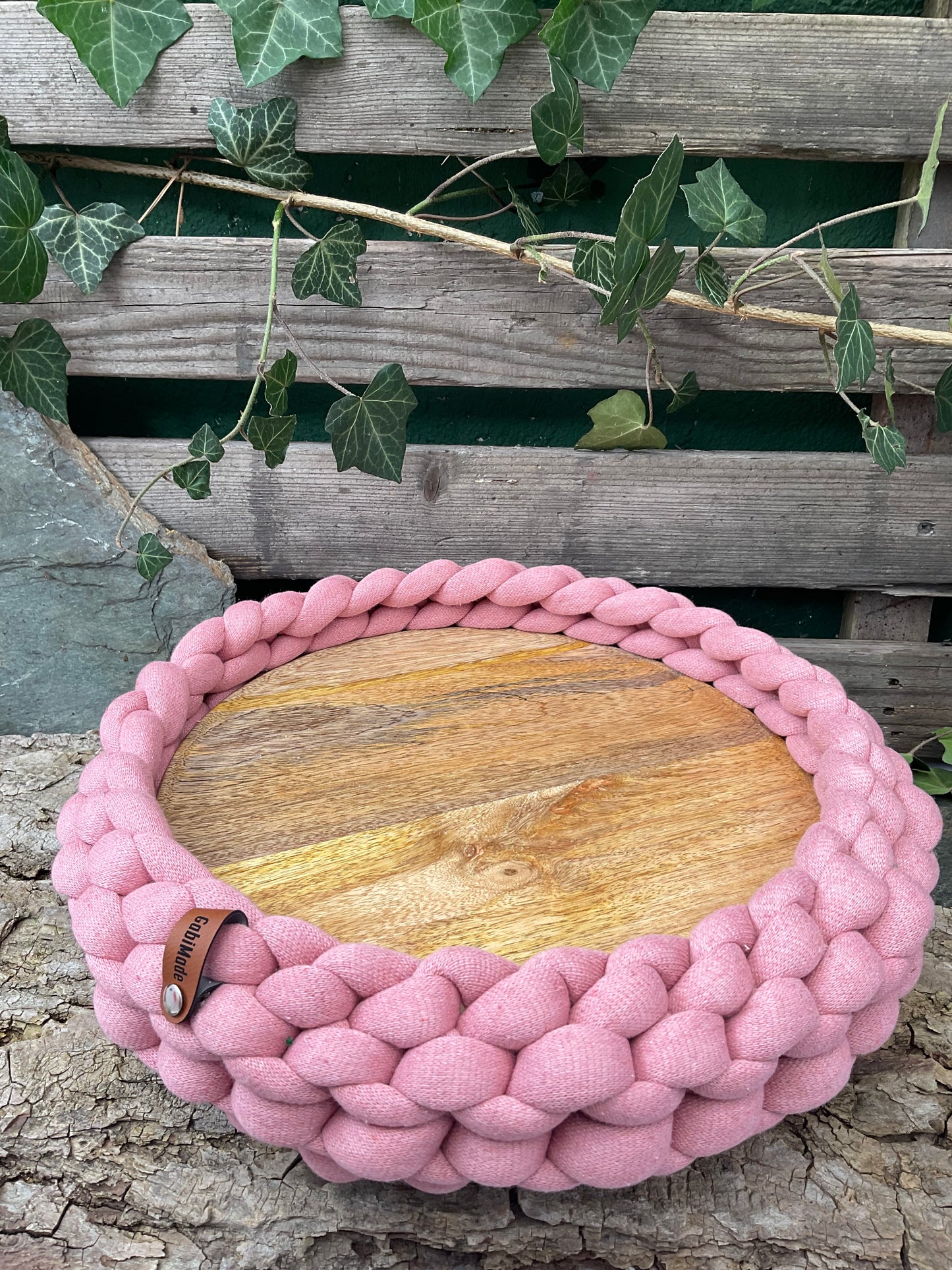 Ein gestricktes rosa Tablett mit Holzteller 