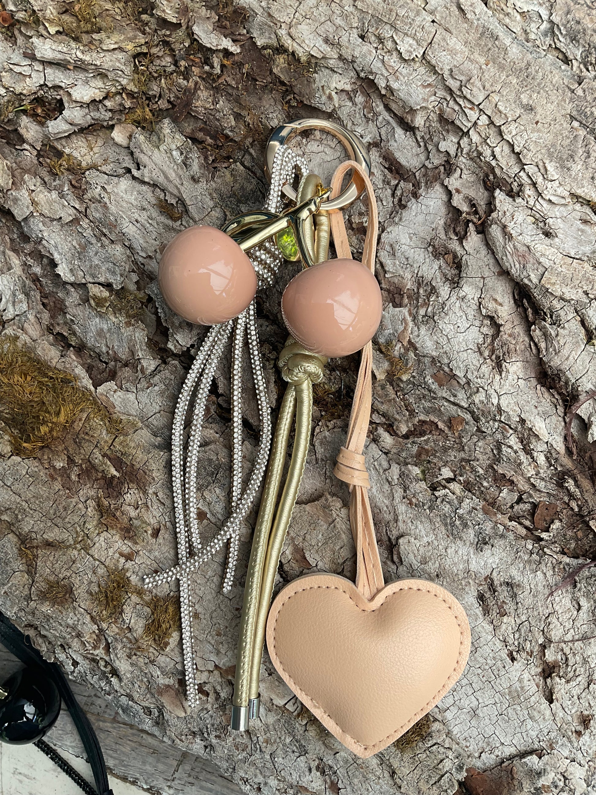 Ein Taschenanhänger in Beige und Gold mit Herz und Kirschen