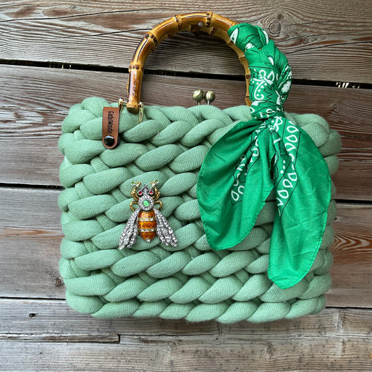Eine gestrickte grüne Trachtentasche mit Brosche und Bambusgriffen 