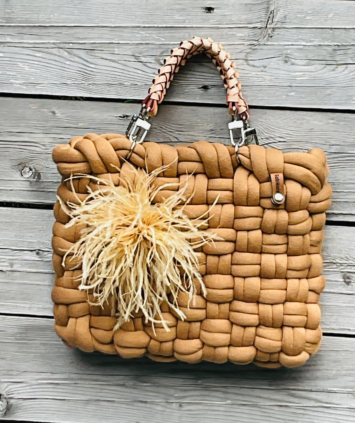 Eine geflochtene Tasche in Cognac mit Ledergriffen und Federbrosche