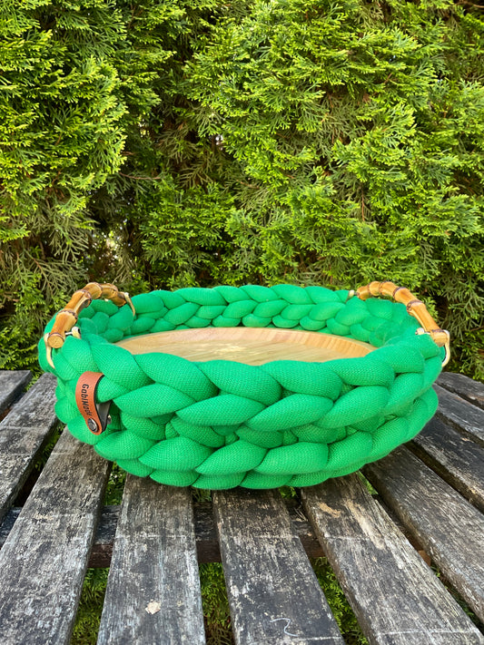 Ein gestricktes grünes Tablett mit Bambusgriffen und einem Holzteller in Medium