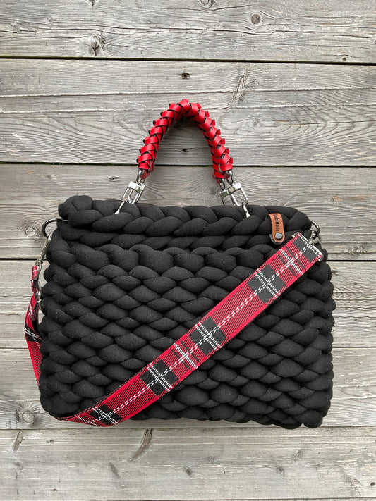 Eine schwarze gestrickte Tasche mit roten Griffen